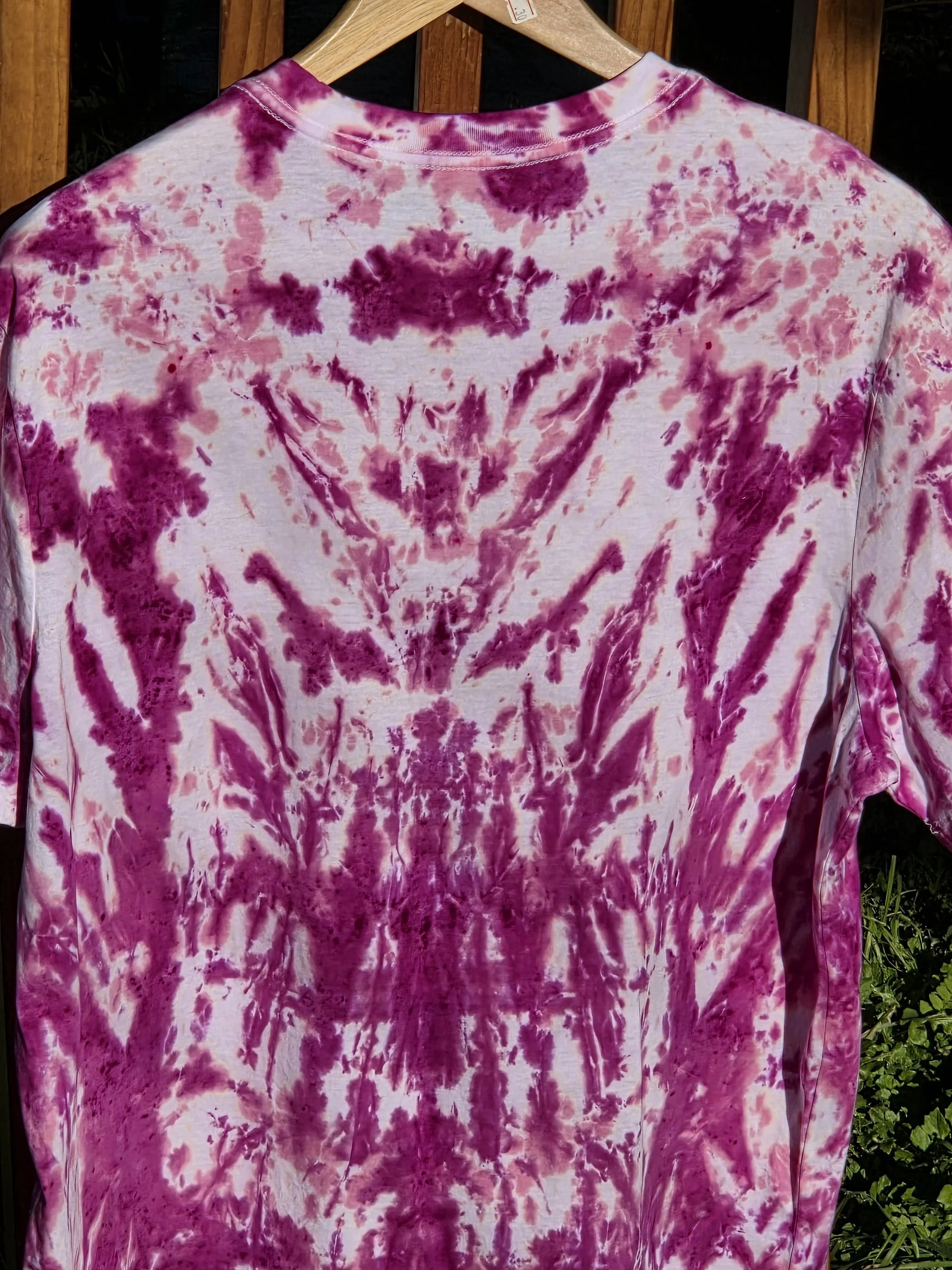 close up back view of A large adult white t-shirt featuring a tie-dye pattern of a deep wine feathery central motif against an abstract pink background.