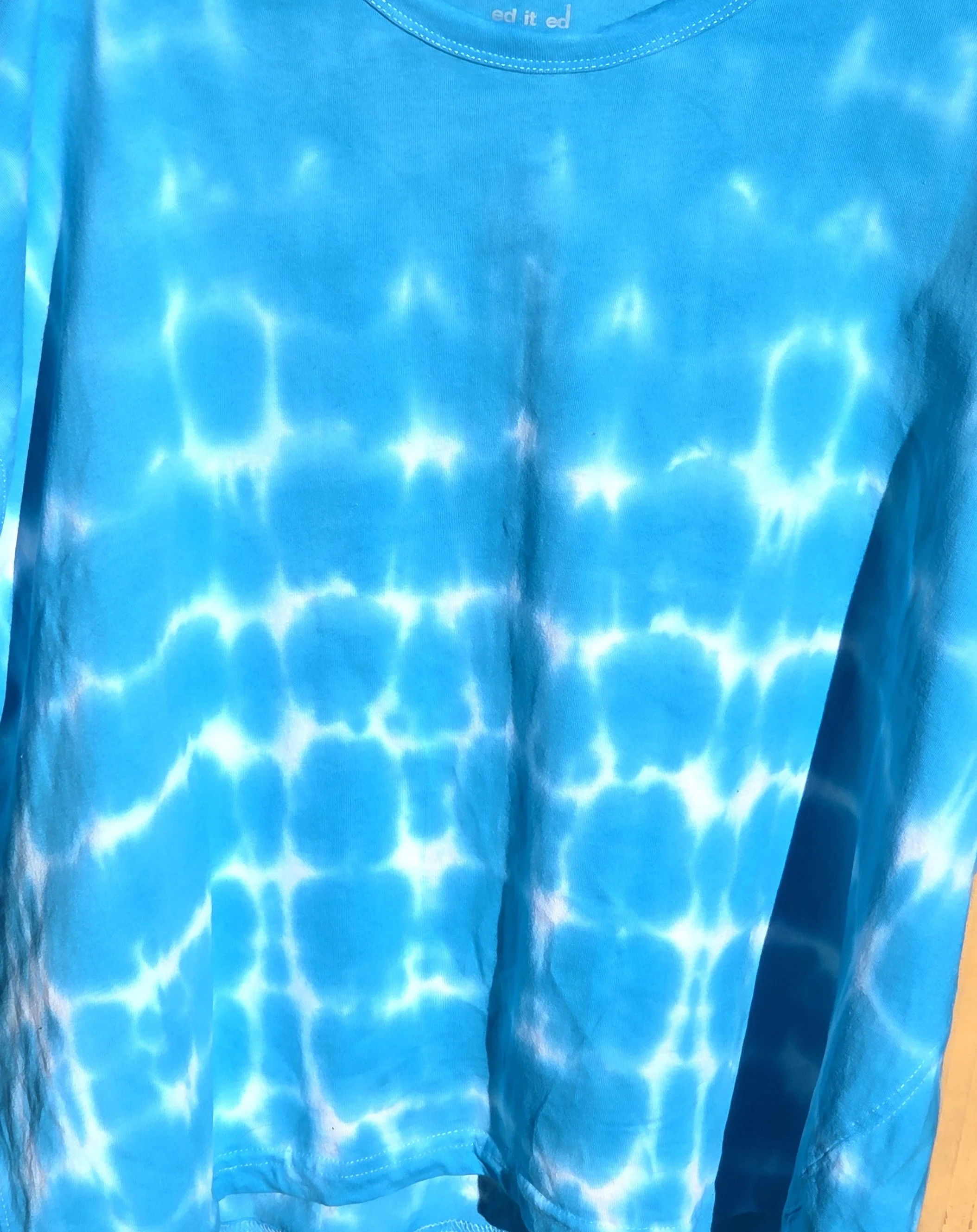 An adult size 12 women's oversized cotton t-shirt featuring a saturated turquoise tie-dye pattern with delicate horizontal white lines.