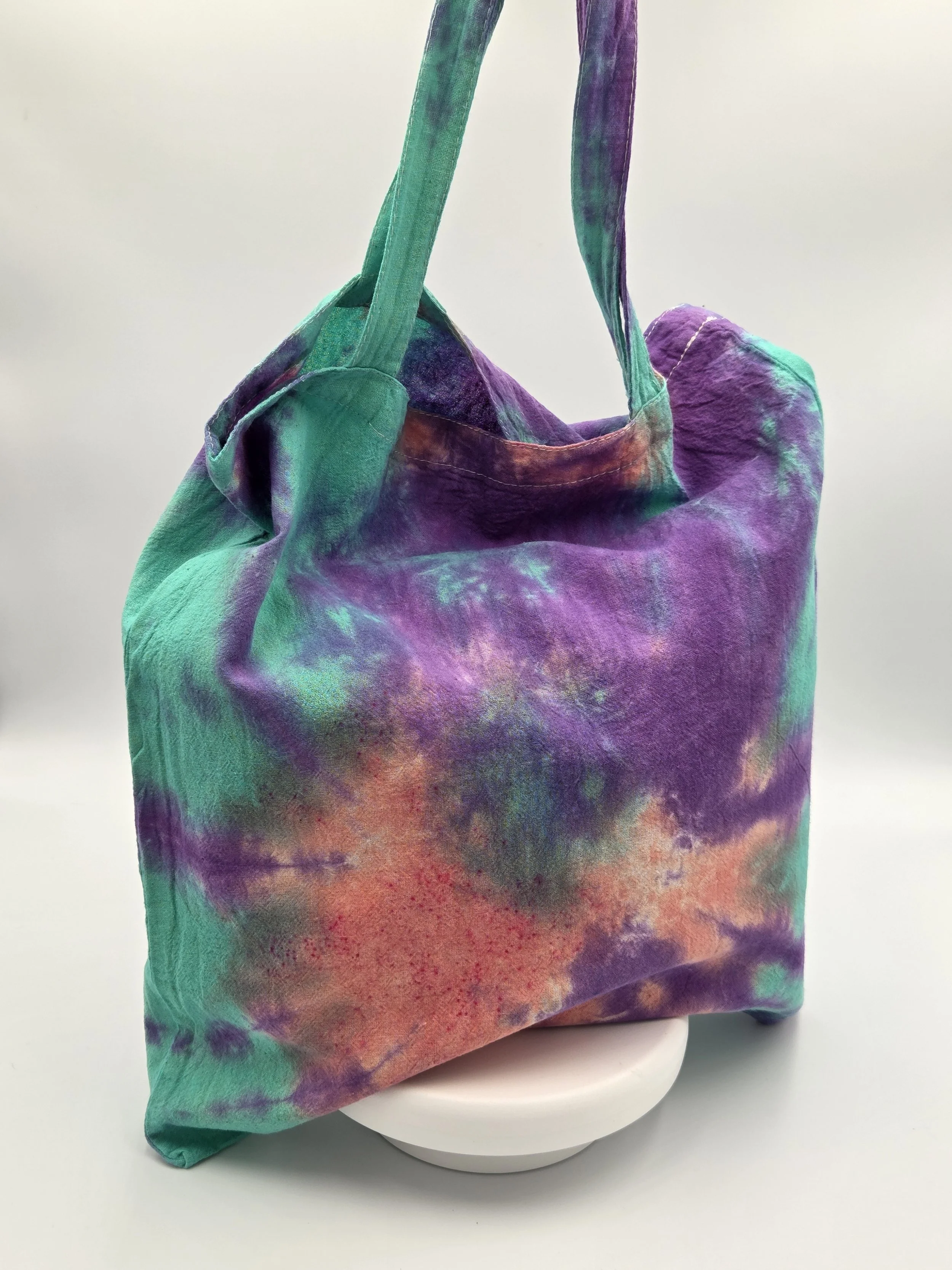 A calico tote bag featuring a tie-dye sea anemone pattern with a coral body and purple arms against a bright teal background.