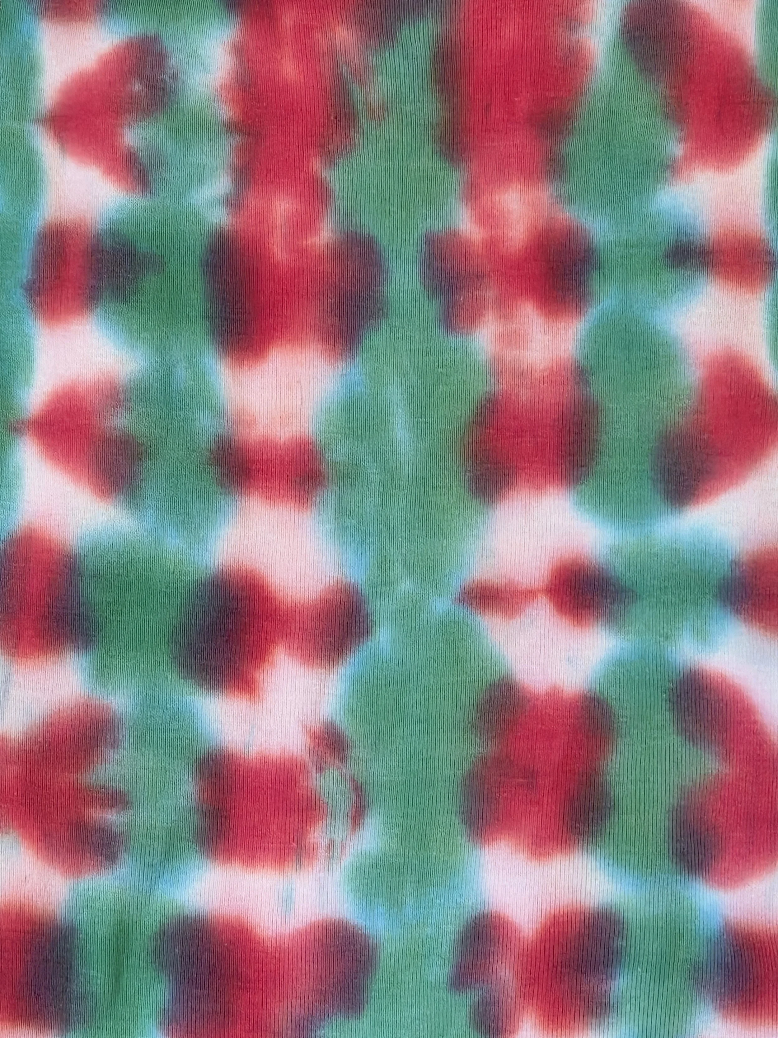 close up of A child's singlet featuring a bold vertical tie-dye pattern of green and red columns with striking white patches down the red sections.