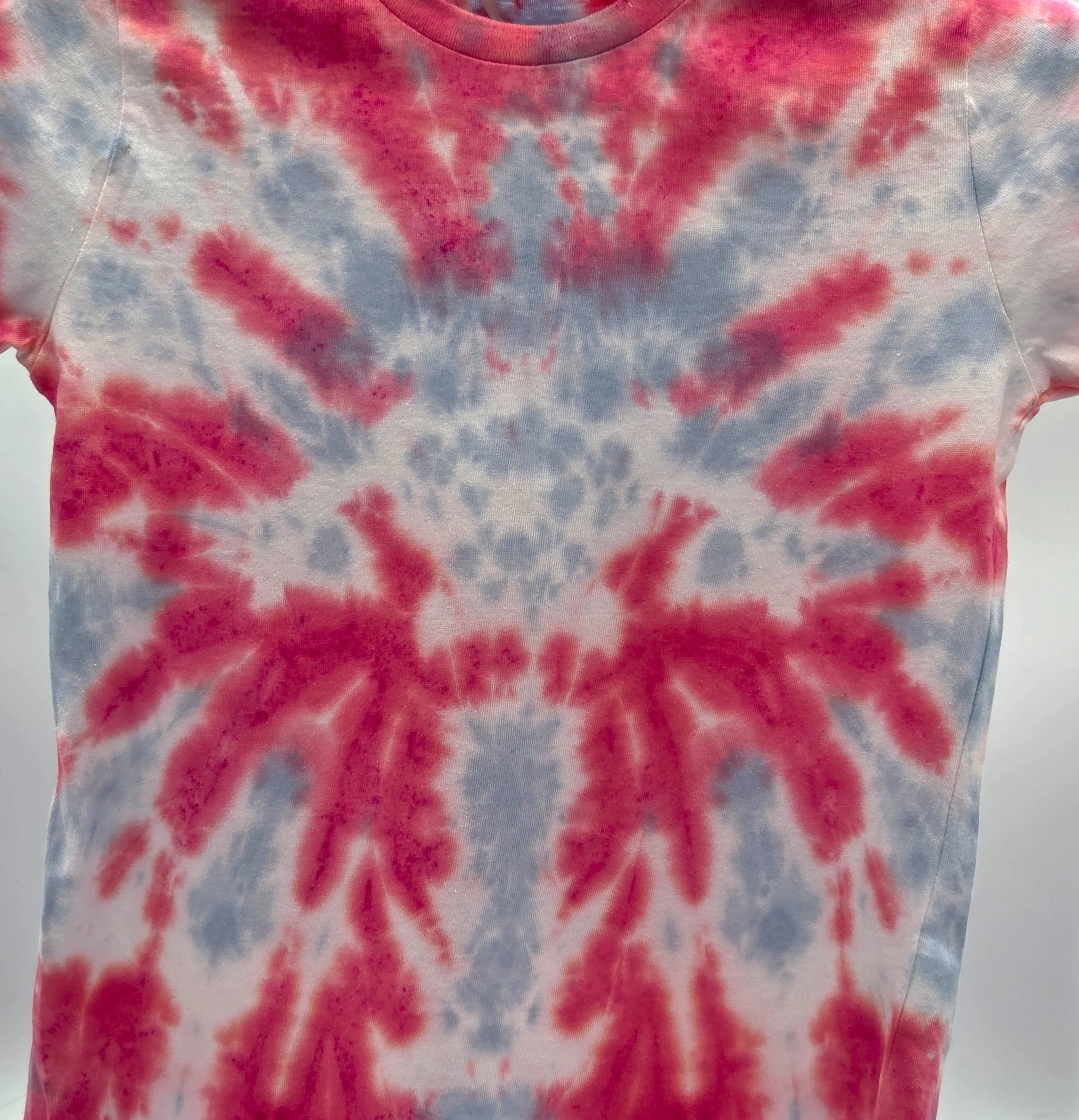 close up of a child's red t-shirt. A central pale grey tie-dye pattern resembles a large webbed flower.