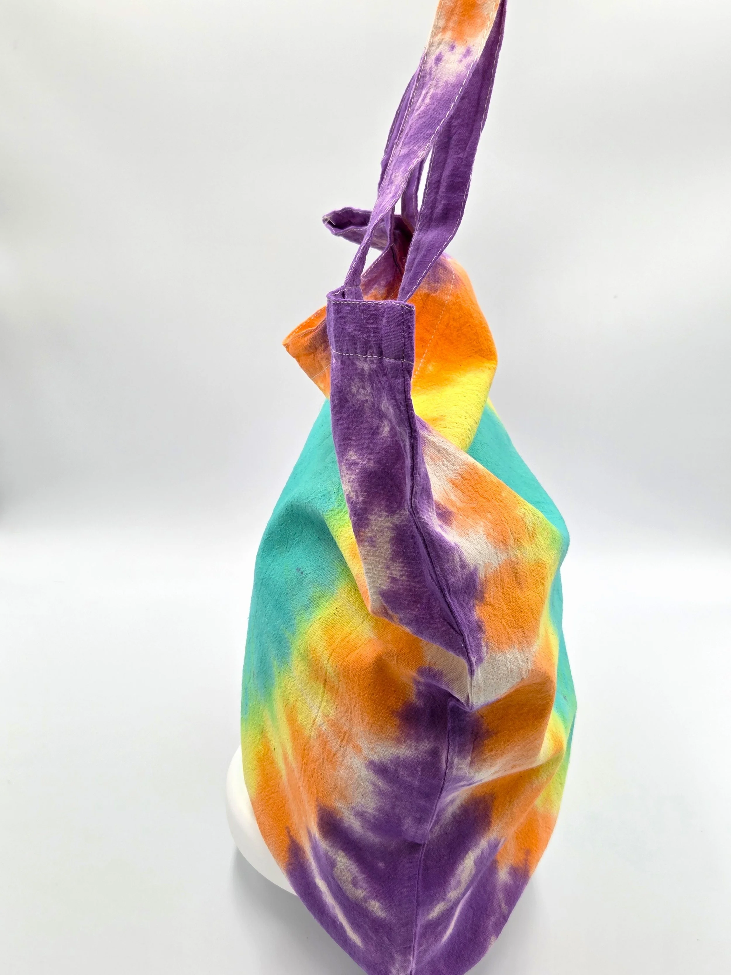 A calico tote bag featuring a tie-dye pattern with a large teal oval center surrounded by glowing rings of yellow, orange, and purple.
