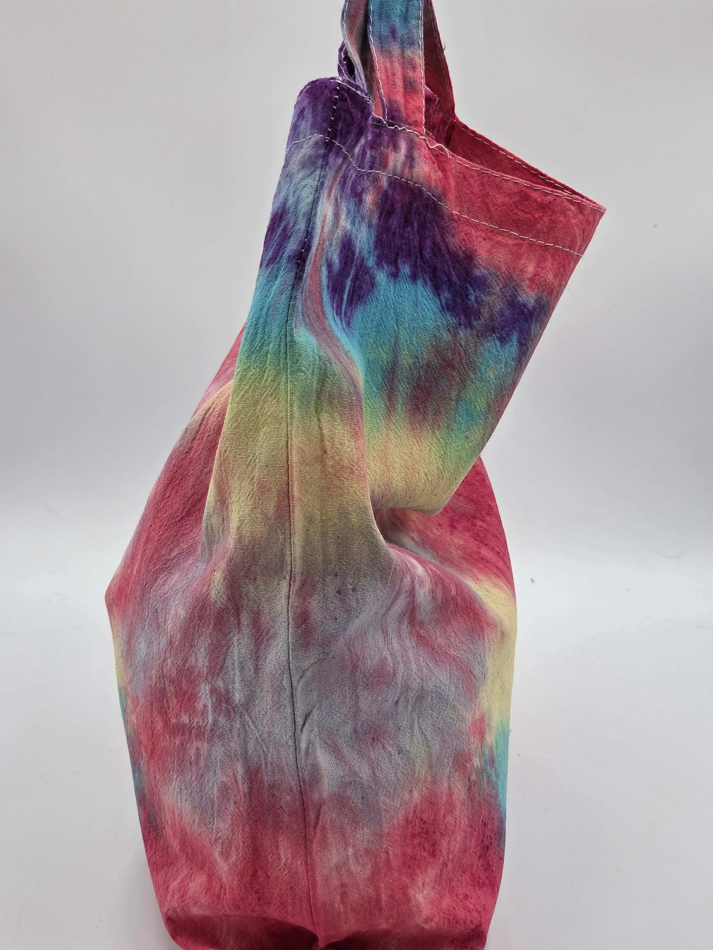 side view A calico tote bag featuring an adaptive tie-dye pattern in coral red, yellow, teal, green, and purple with a playful crab-inspired central motif.