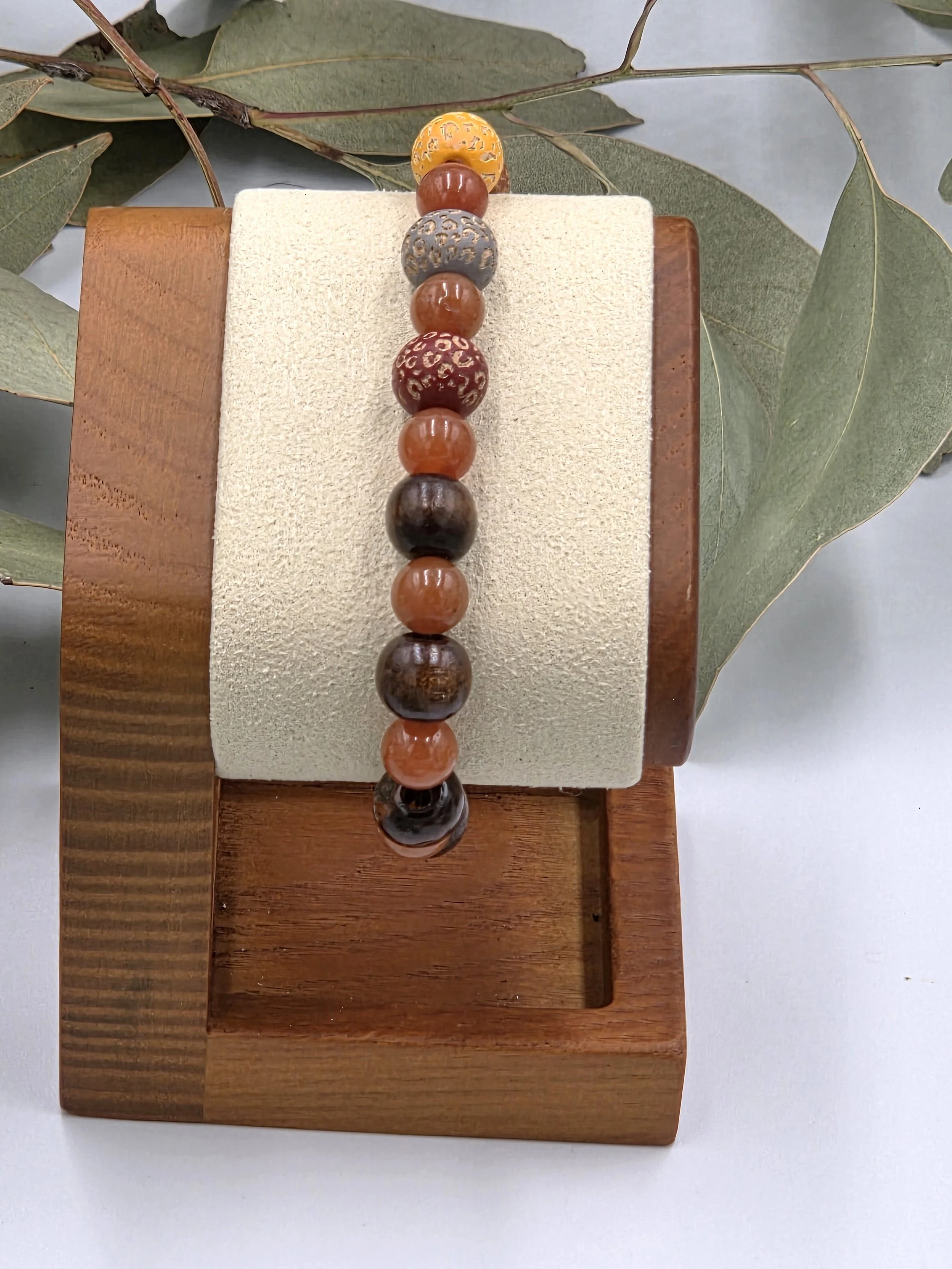 Warm red aventurine beads alternating with multi-coloured leopard print wood beads and dark brown wood beads on an elastic bracelet.