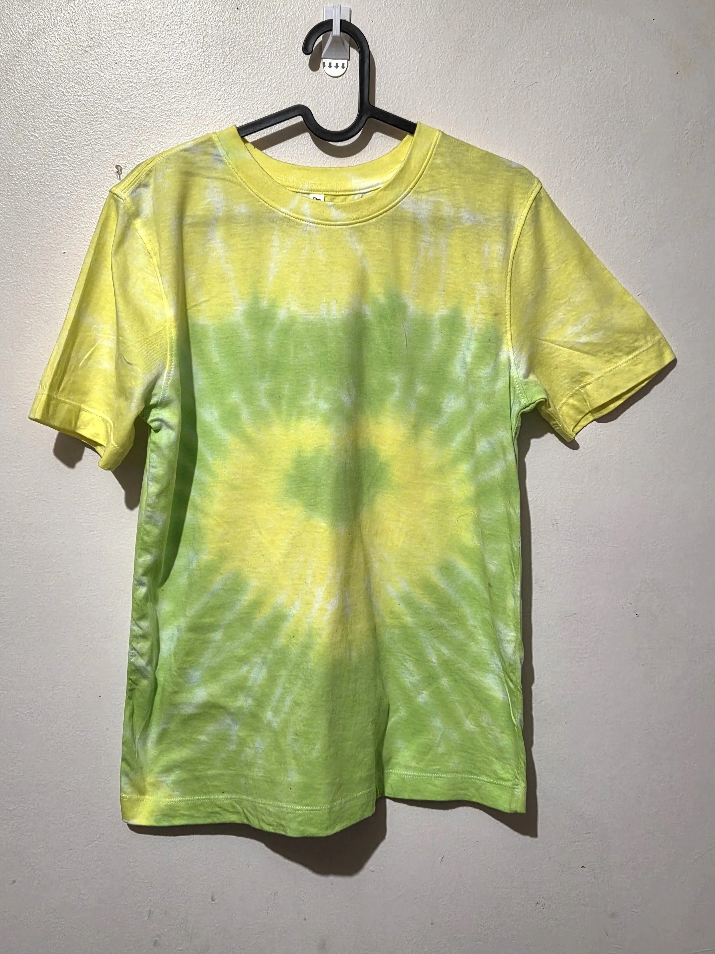 An adult size 10 women's cotton t-shirt featuring a tie-dye heart pattern in subtle pastel yellow and lime green.