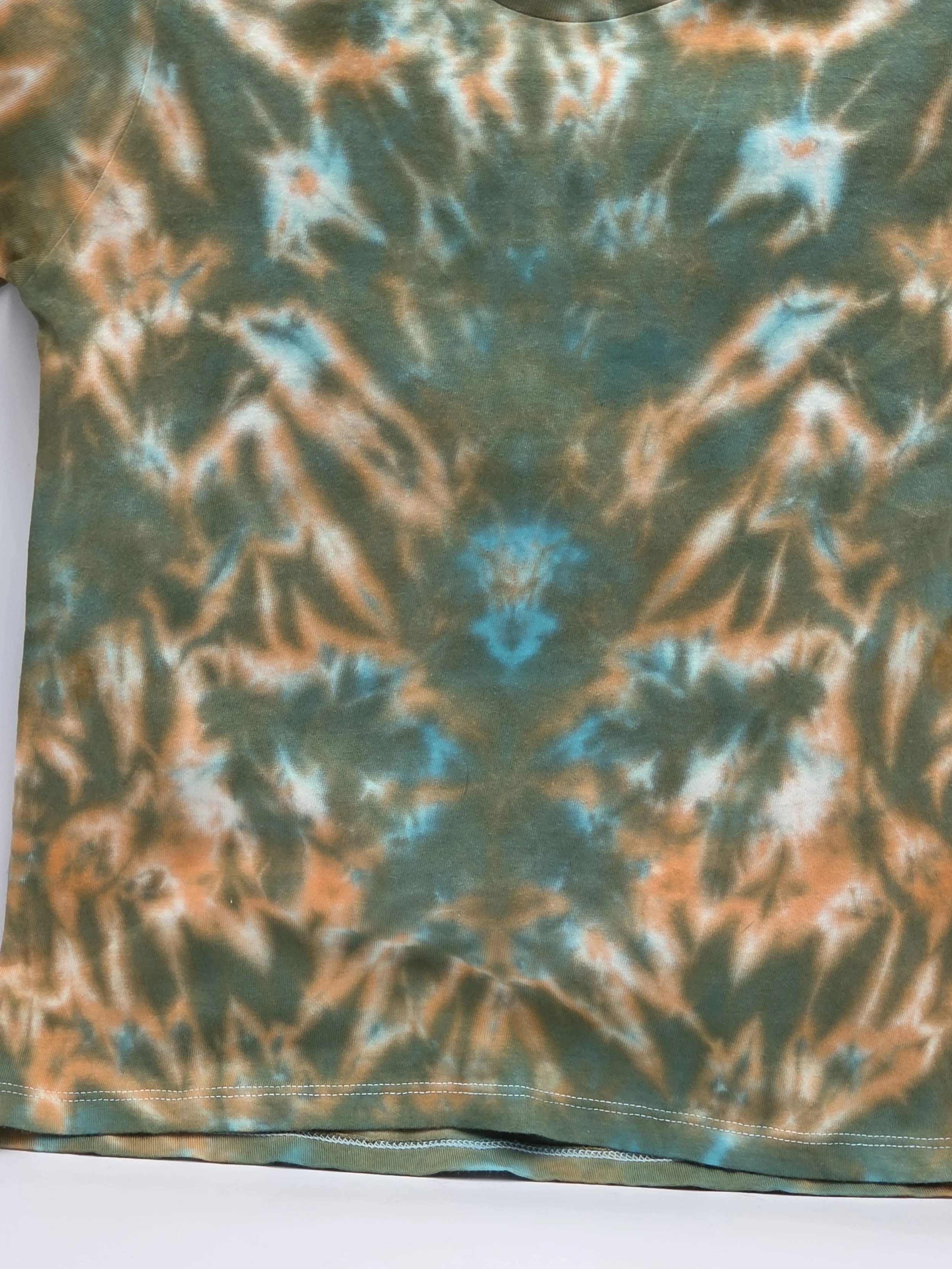 clos up of A child's size 6 t-shirt featuring a soft, pastel tie-dye tiger stripe pattern of khaki and orange with hints of sky blue.