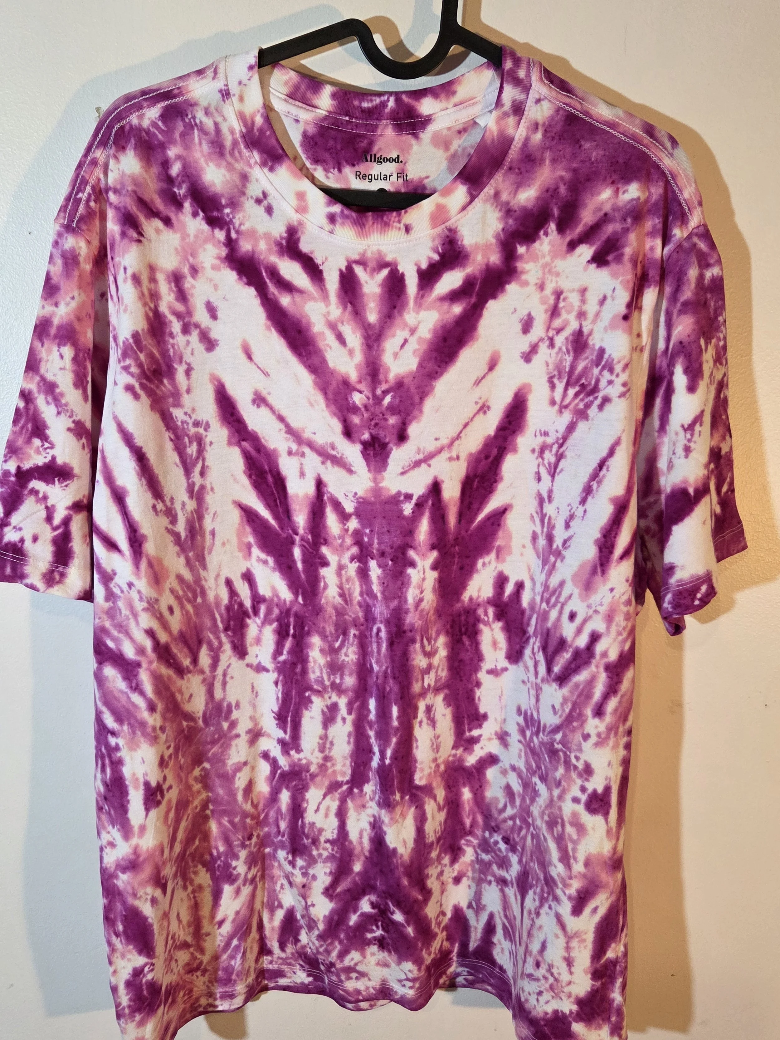 A large adult white t-shirt featuring a tie-dye pattern of a deep wine feathery central motif against an abstract pink background.