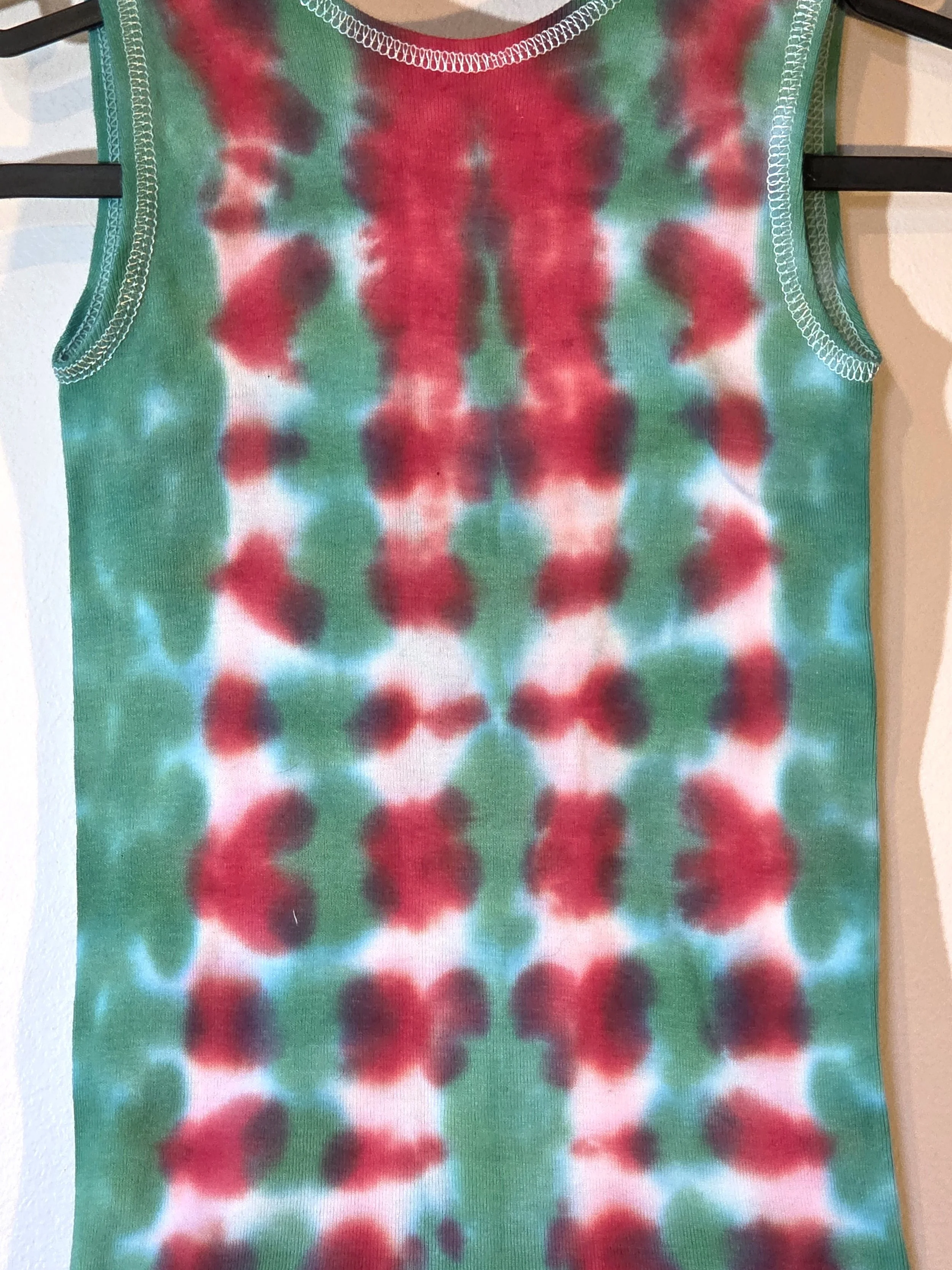 back view of A child's singlet featuring a bold vertical tie-dye pattern of green and red columns with striking white patches down the red sections.