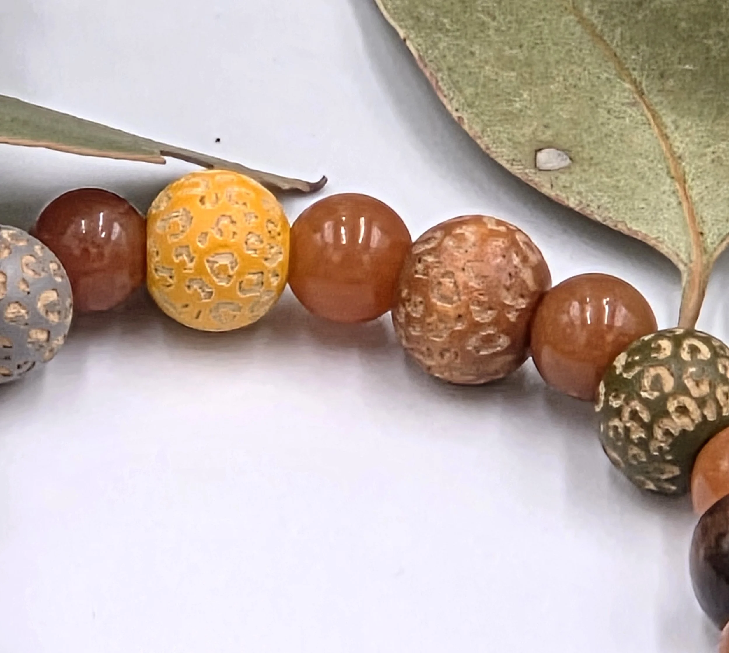 close up of Warm red aventurine beads alternating with multi-coloured leopard print wood beads and dark brown wood beads on an elastic bracelet.