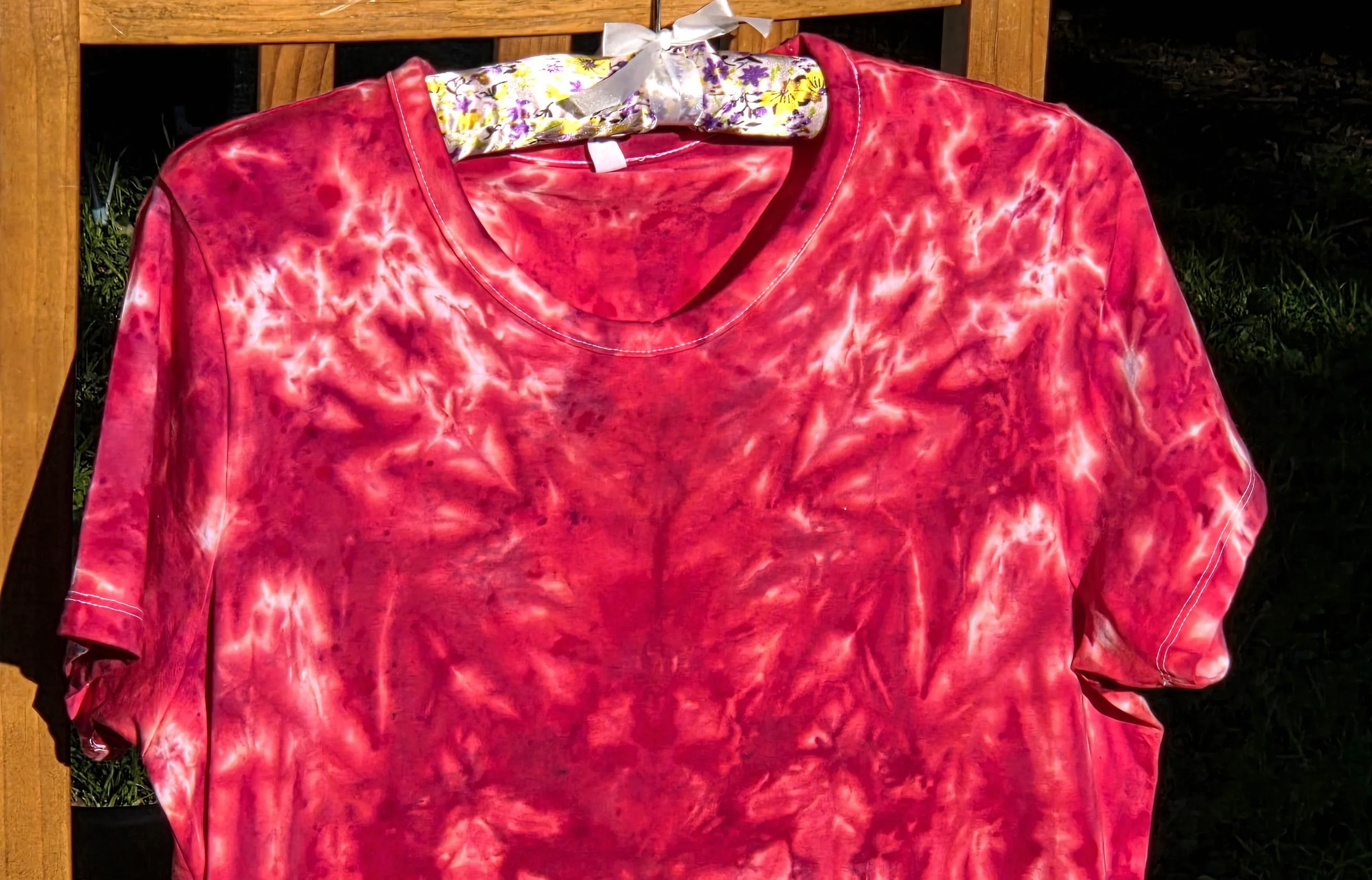 close up of A size 14 women's t-shirt featuring a highly saturated red and coral tie-dye pattern of abstract swirls radiating from the center.