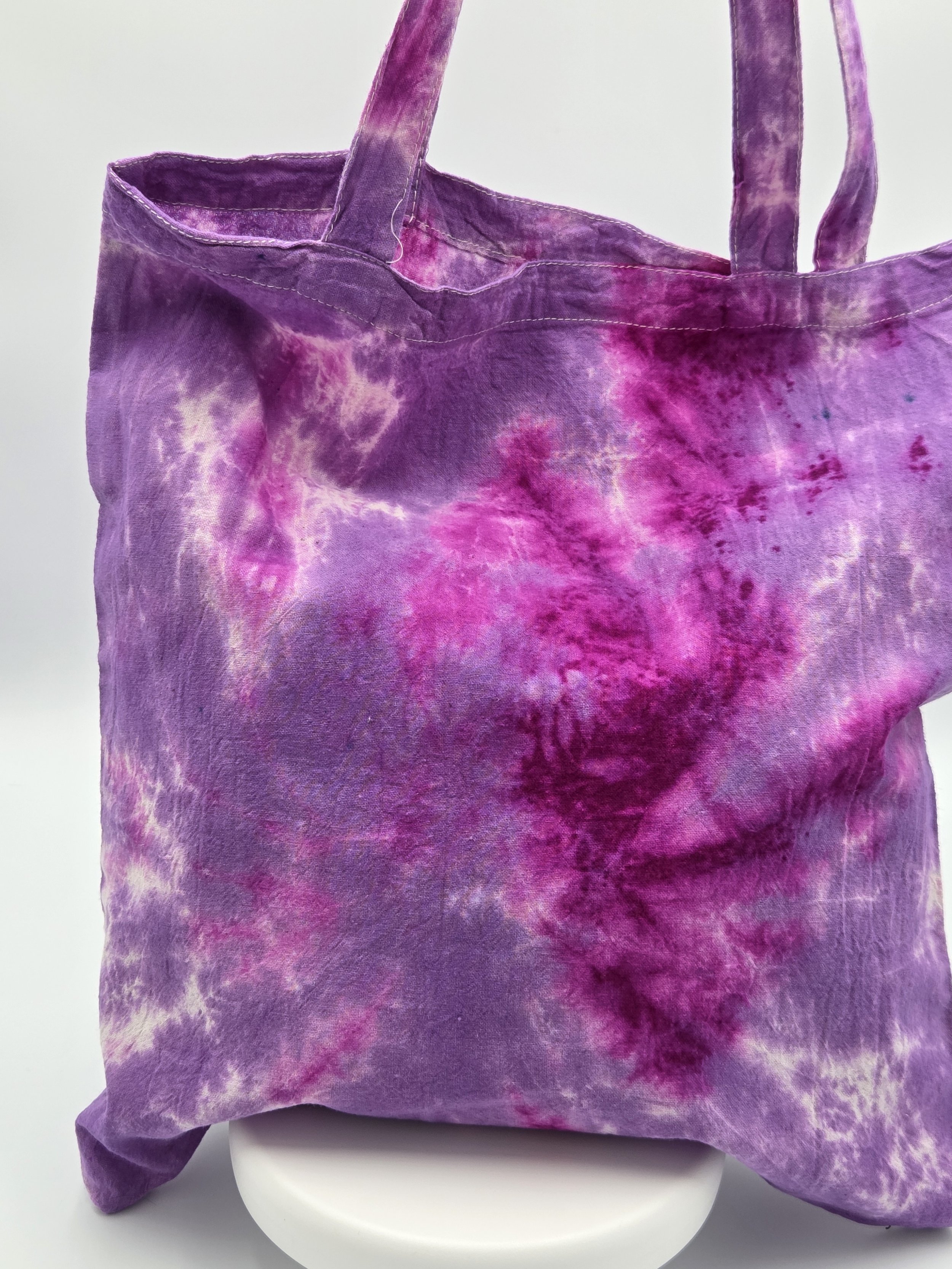 A calico tote bag featuring a tie-dye lotus flower pattern in deep fuchsia resting against a rich purple and white background.
