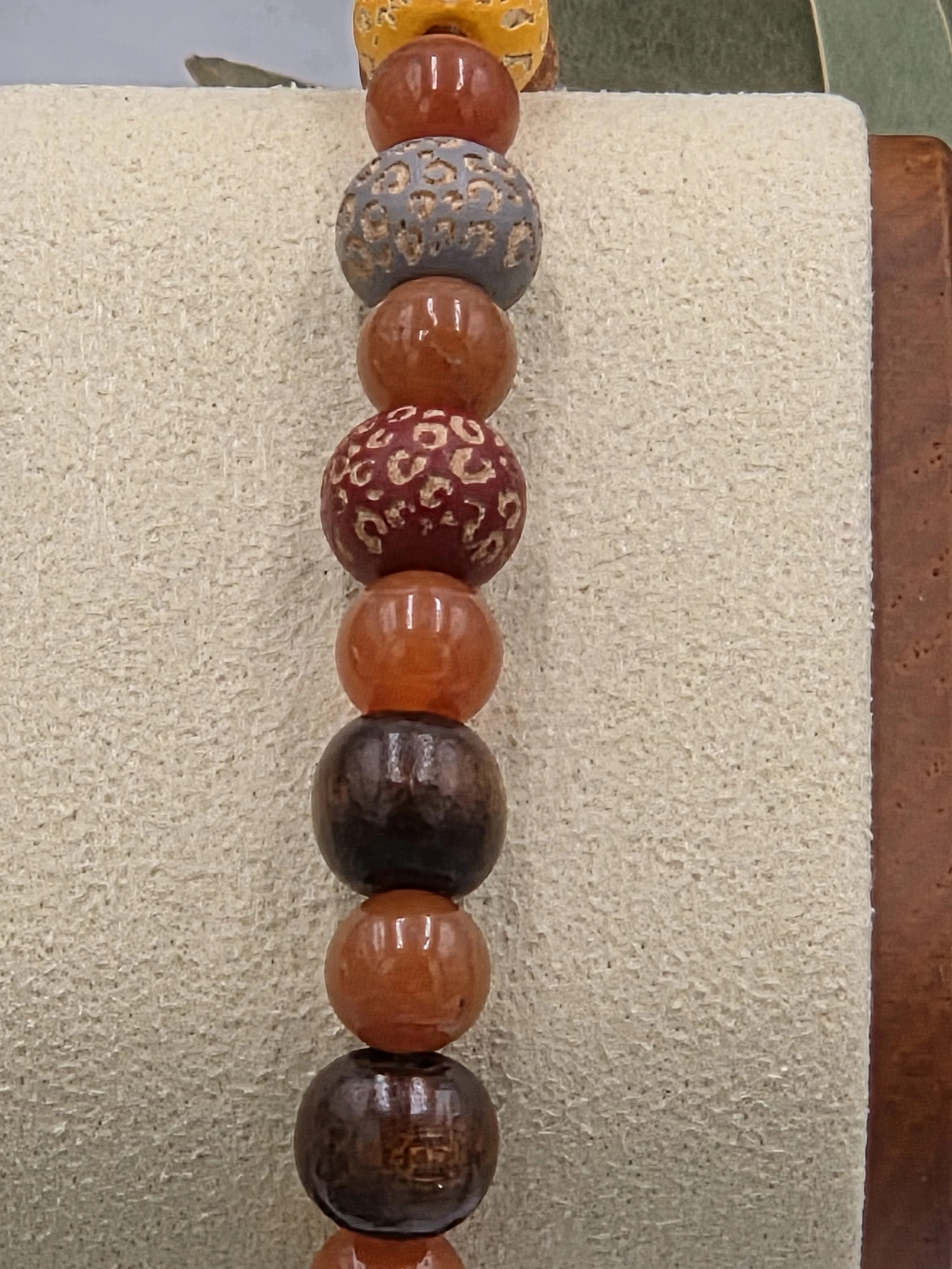 close up of Warm red aventurine beads alternating with multi-coloured leopard print wood beads and dark brown wood beads on an elastic bracelet.