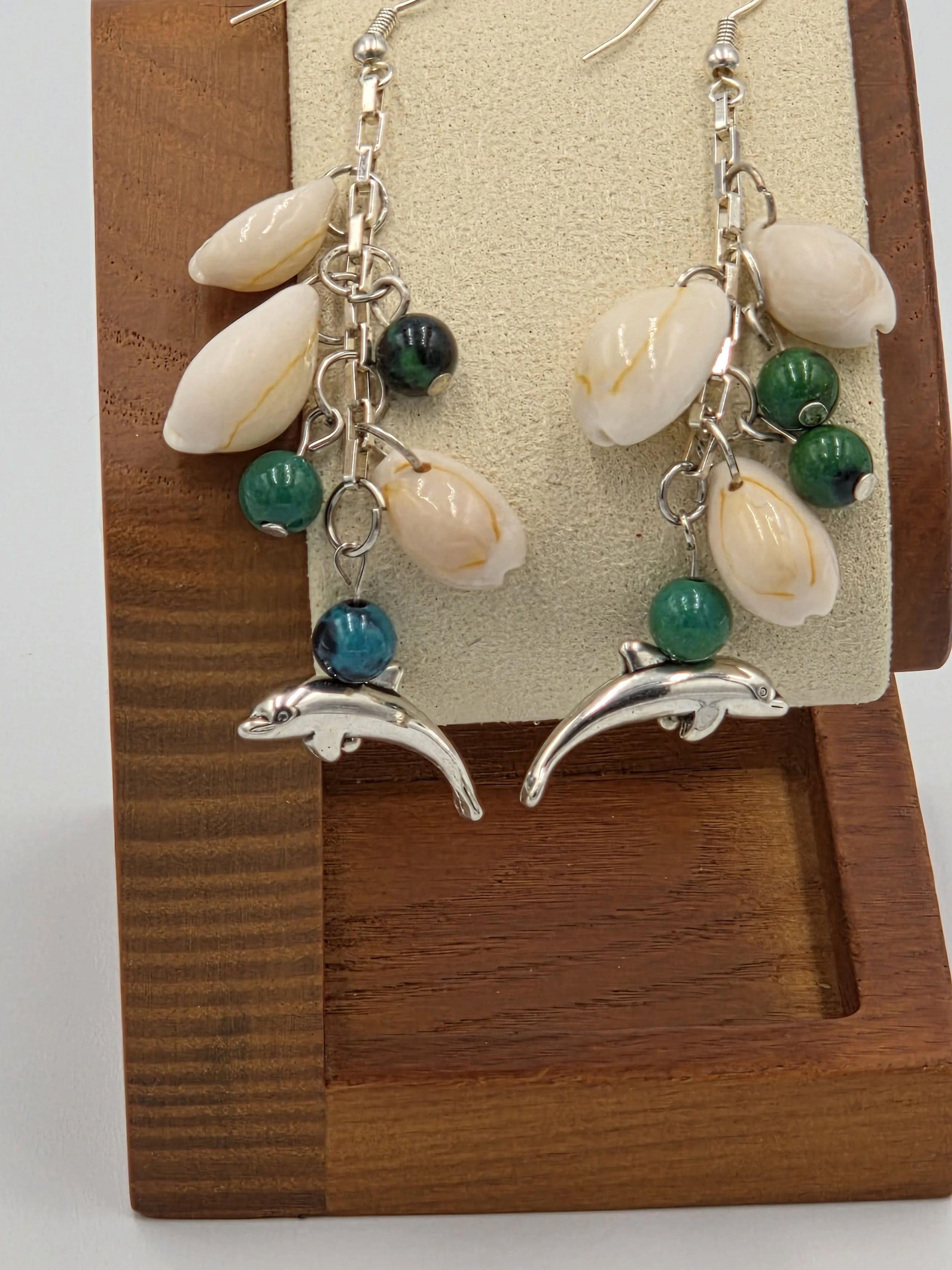 Long silver chain earrings with three cowrie shells, three blue-green gemstones, and dolphin charms.
