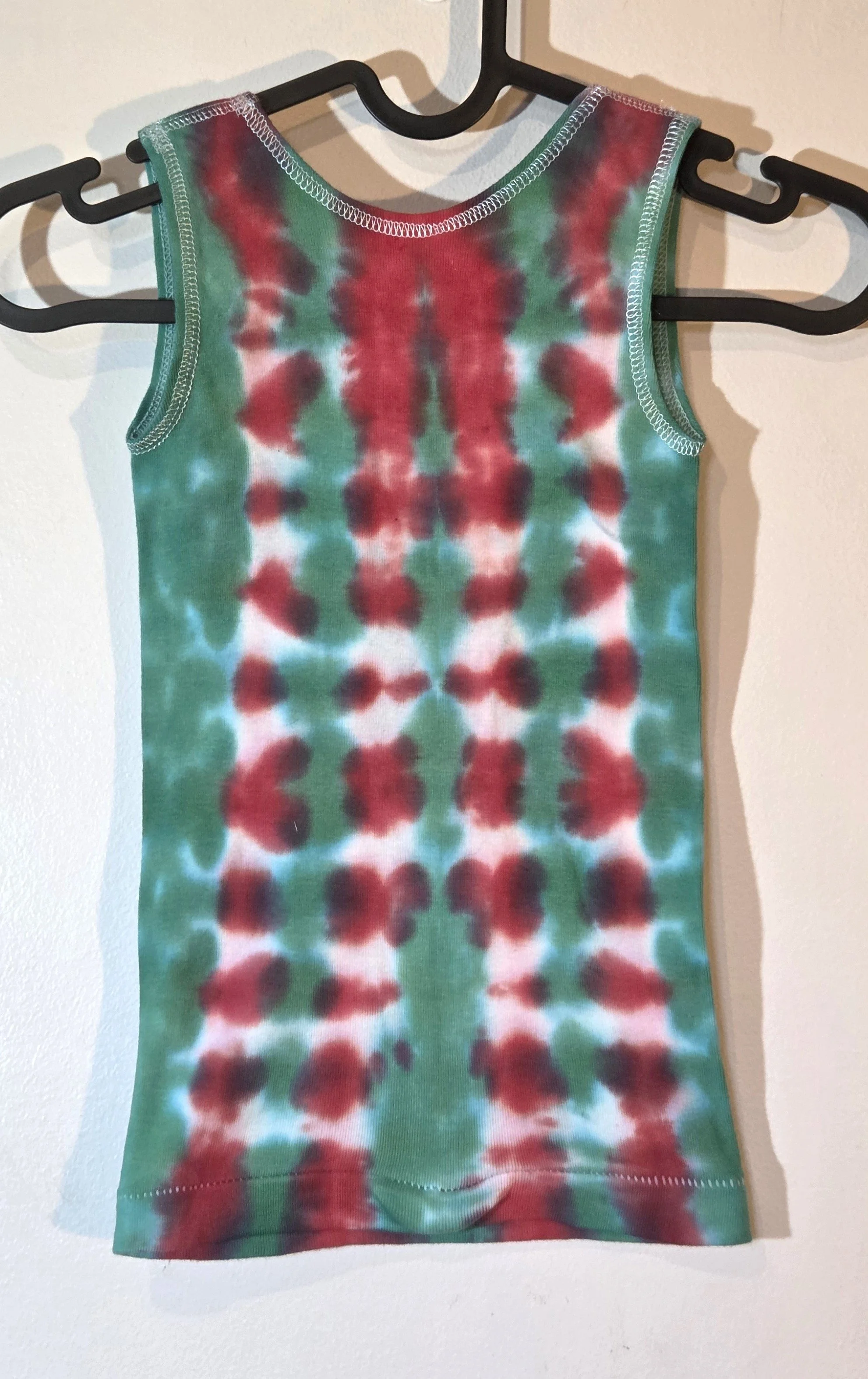 back view of A child's singlet featuring a bold vertical tie-dye pattern of green and red columns with striking white patches down the red sections.