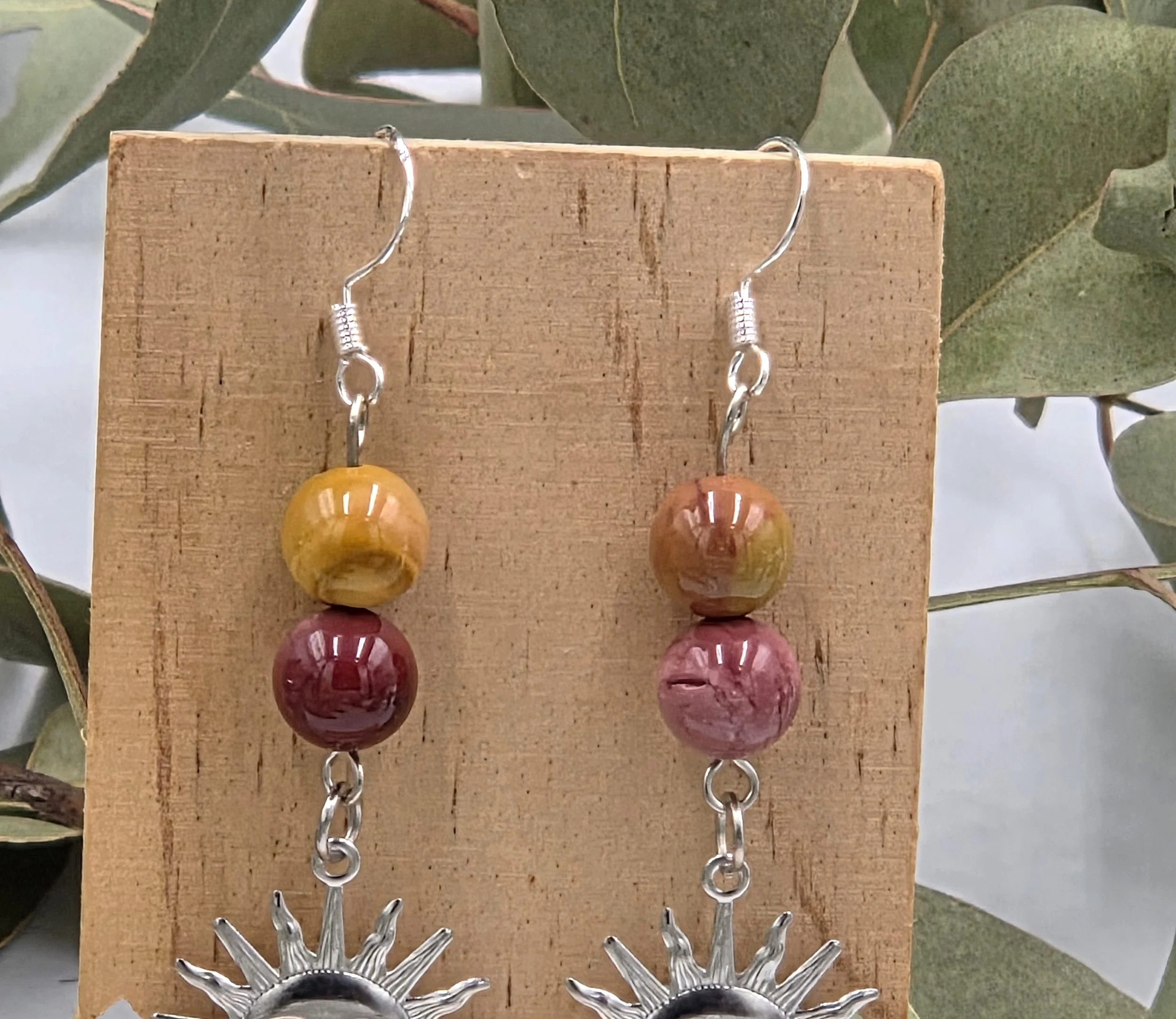 Reddish-brown Mookaite beads with a silver sun face charm on sterling silver dangle earring hooks.