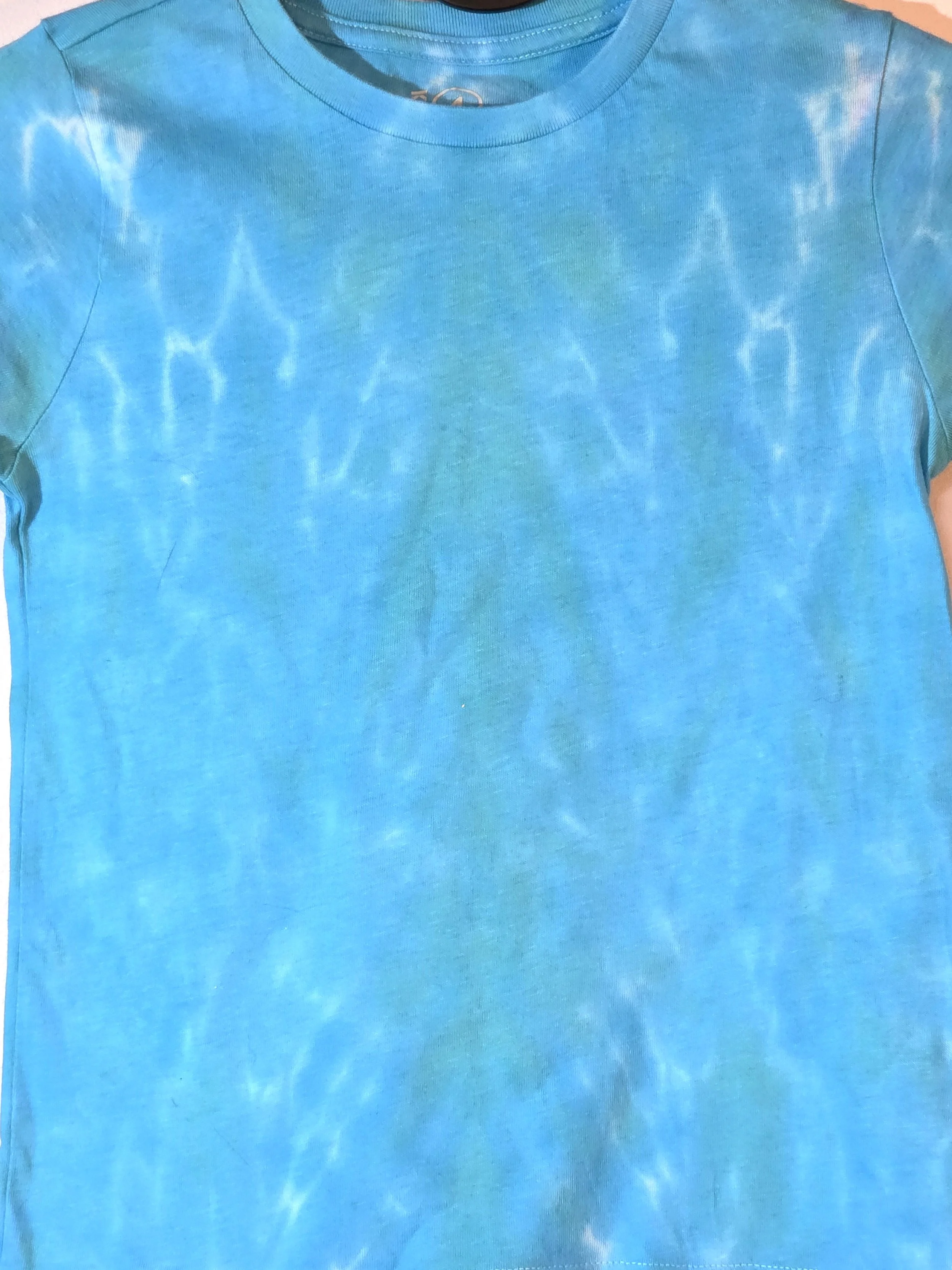 close up of A child's sky blue t-shirt displaying a delicate, flowing tiger stripe tie-dye pattern with thin white veins near the shoulders.