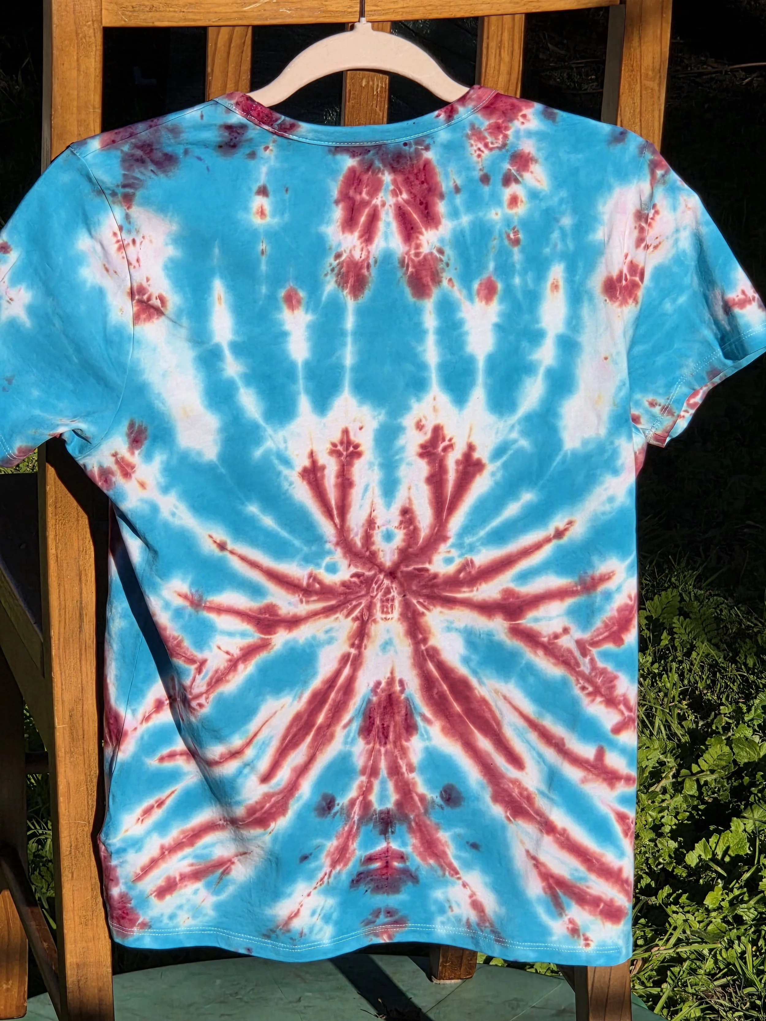 A size 10 t-shirt featuring a tie-dye pattern of a sharp, spiky purple and wine flower on a sky blue and white background.