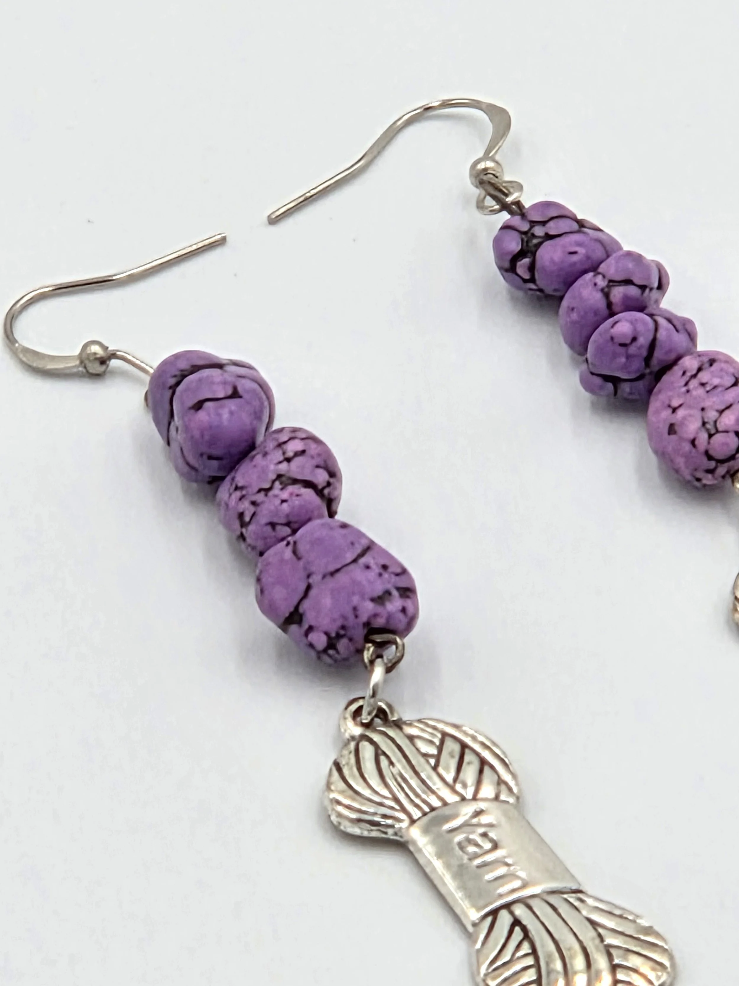 close up of Long silver earrings with purple stone nuggets and a silver yarn charm on silver hooks.