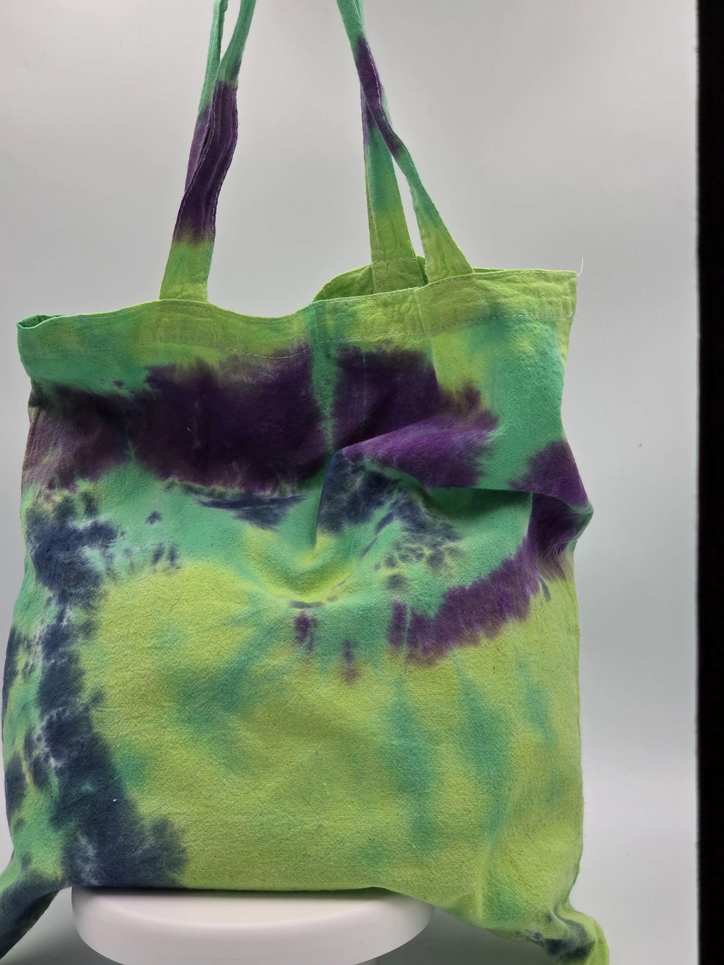 A calico tote bag featuring an abstract dark blue and purple half-circle tie-dye pattern against a lime green and pastel yellow background.