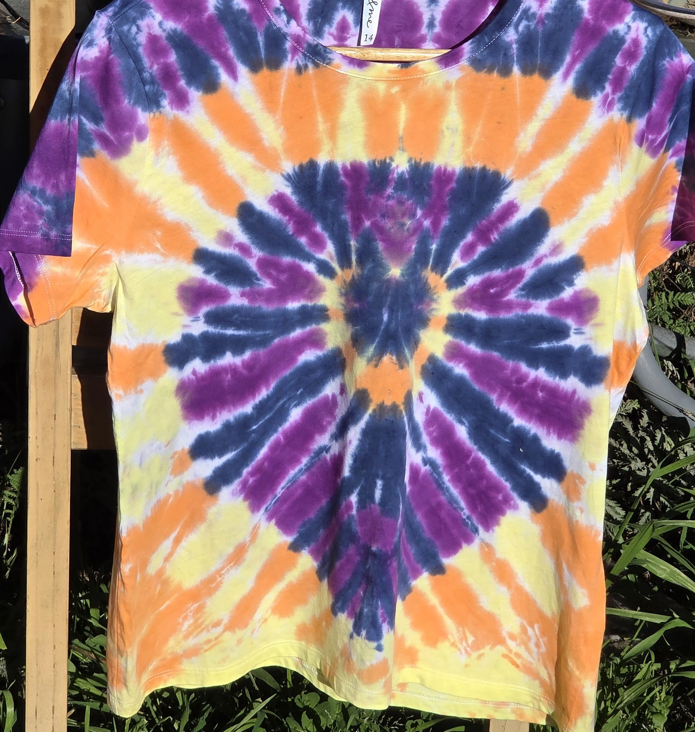 An adult size 14 women's cotton t-shirt featuring a tie-dye sunburst design in purple, dark blue, yellow, and orange.