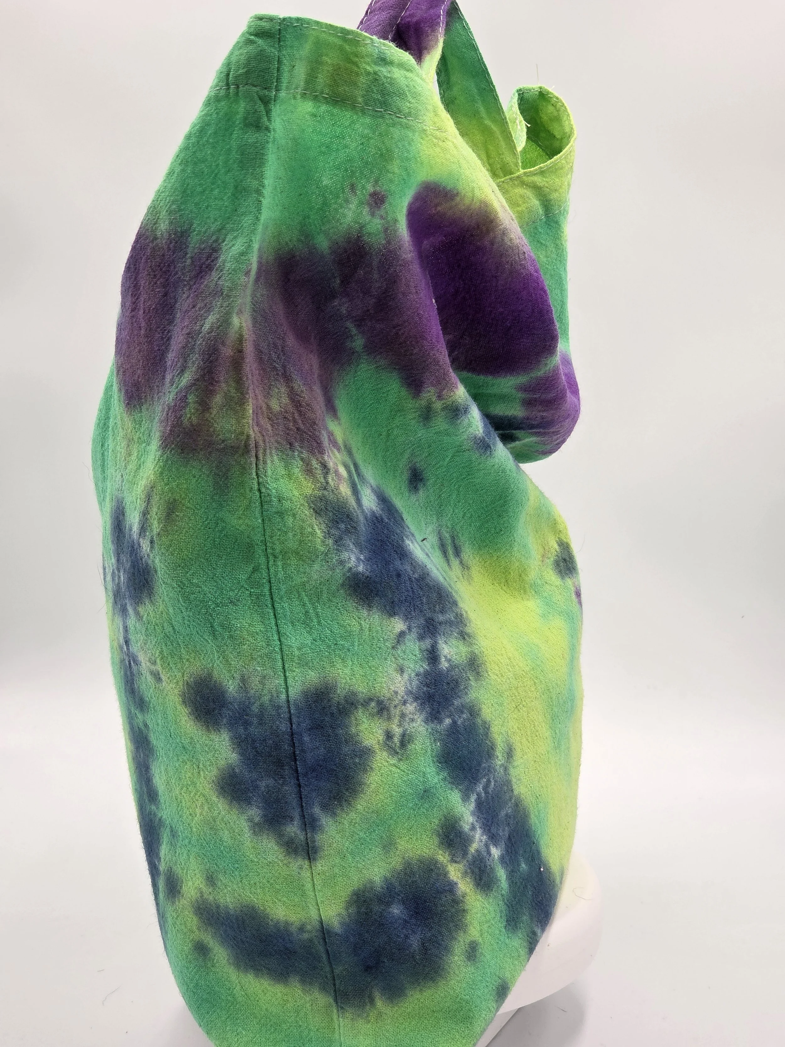 A calico tote bag featuring an abstract dark blue and purple half-circle tie-dye pattern against a lime green and pastel yellow background.