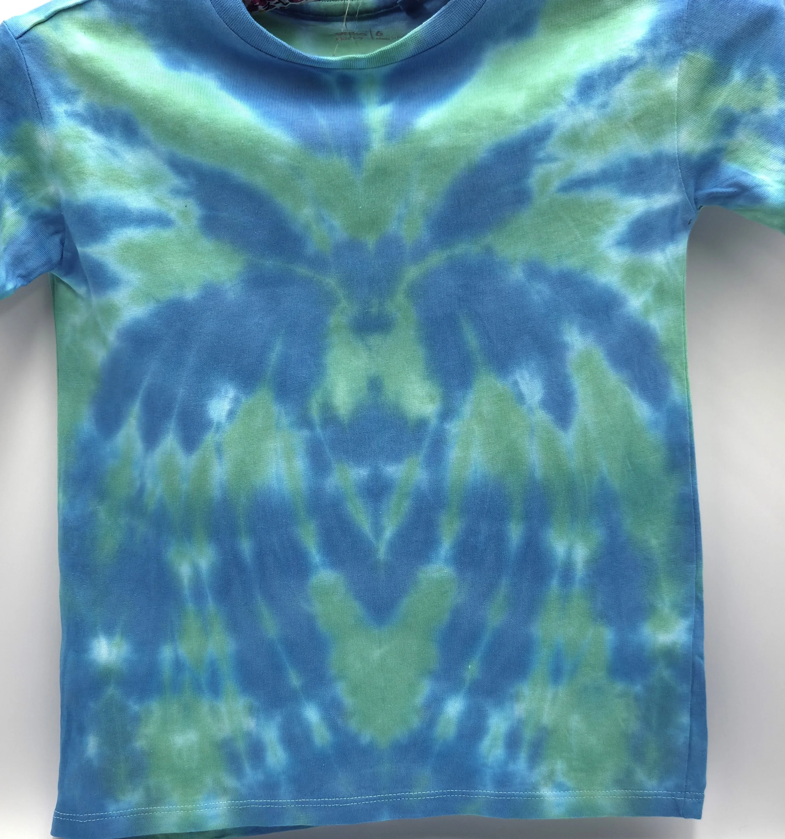 close up of A child's light green t-shirt displaying a central sky blue tie-dye spider pattern, front view