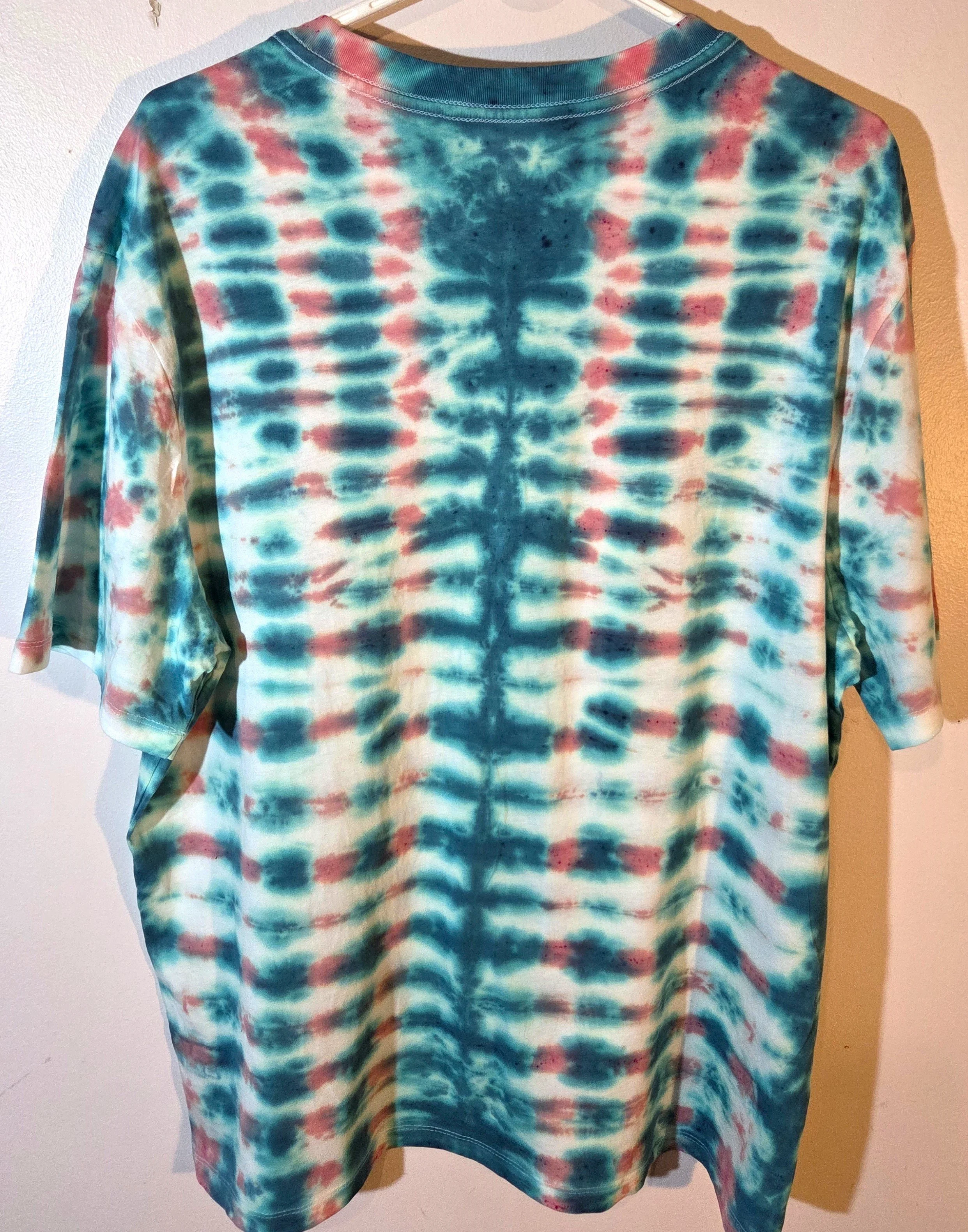 back view of An XL adult white t-shirt featuring a tie-dye grid of Aegean green and coral with a prominent green centerline and eye motif near the neck.