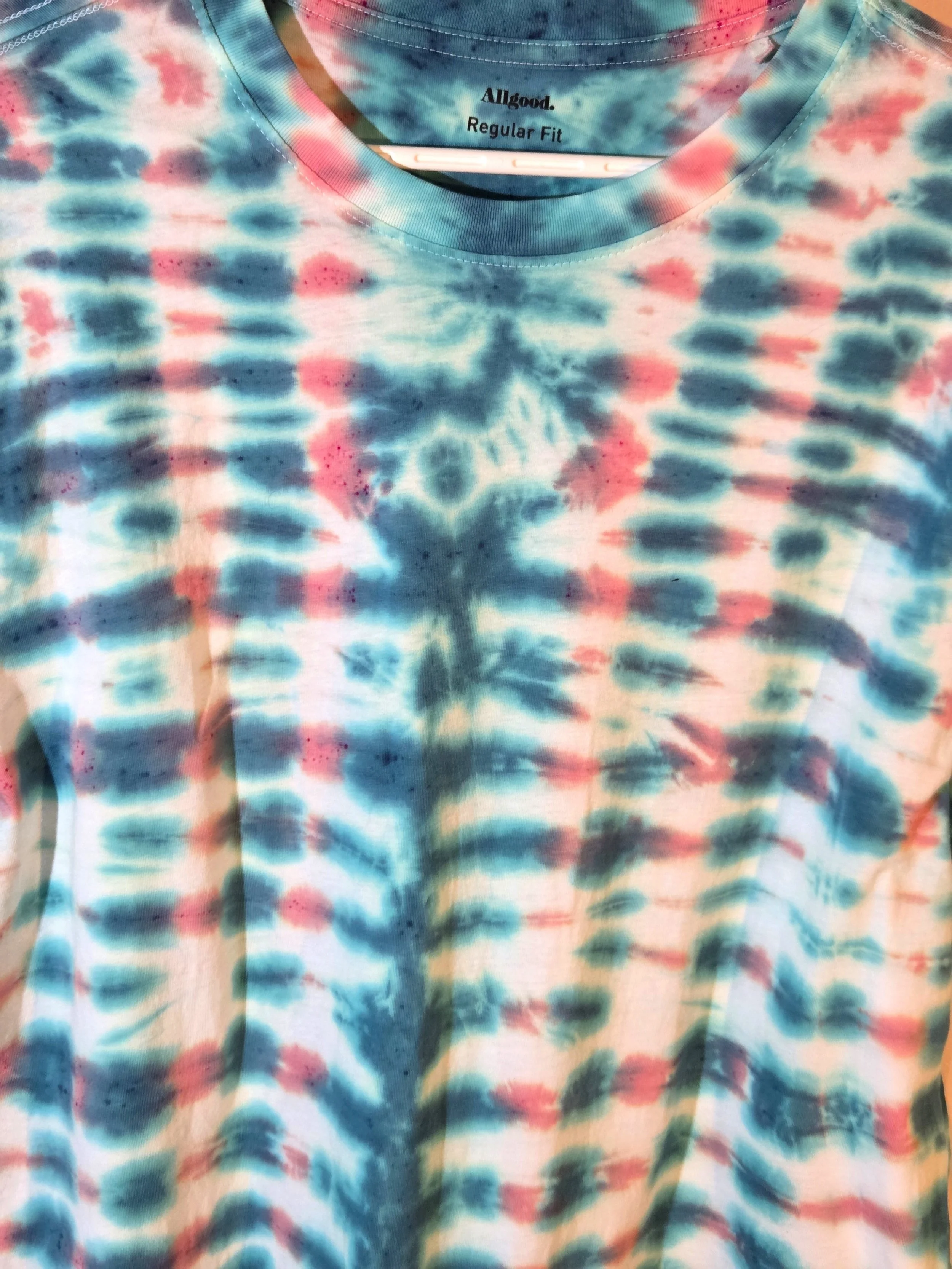 close up of An XL adult white t-shirt featuring a tie-dye grid of Aegean green and coral with a prominent green centerline and eye motif near the neck.