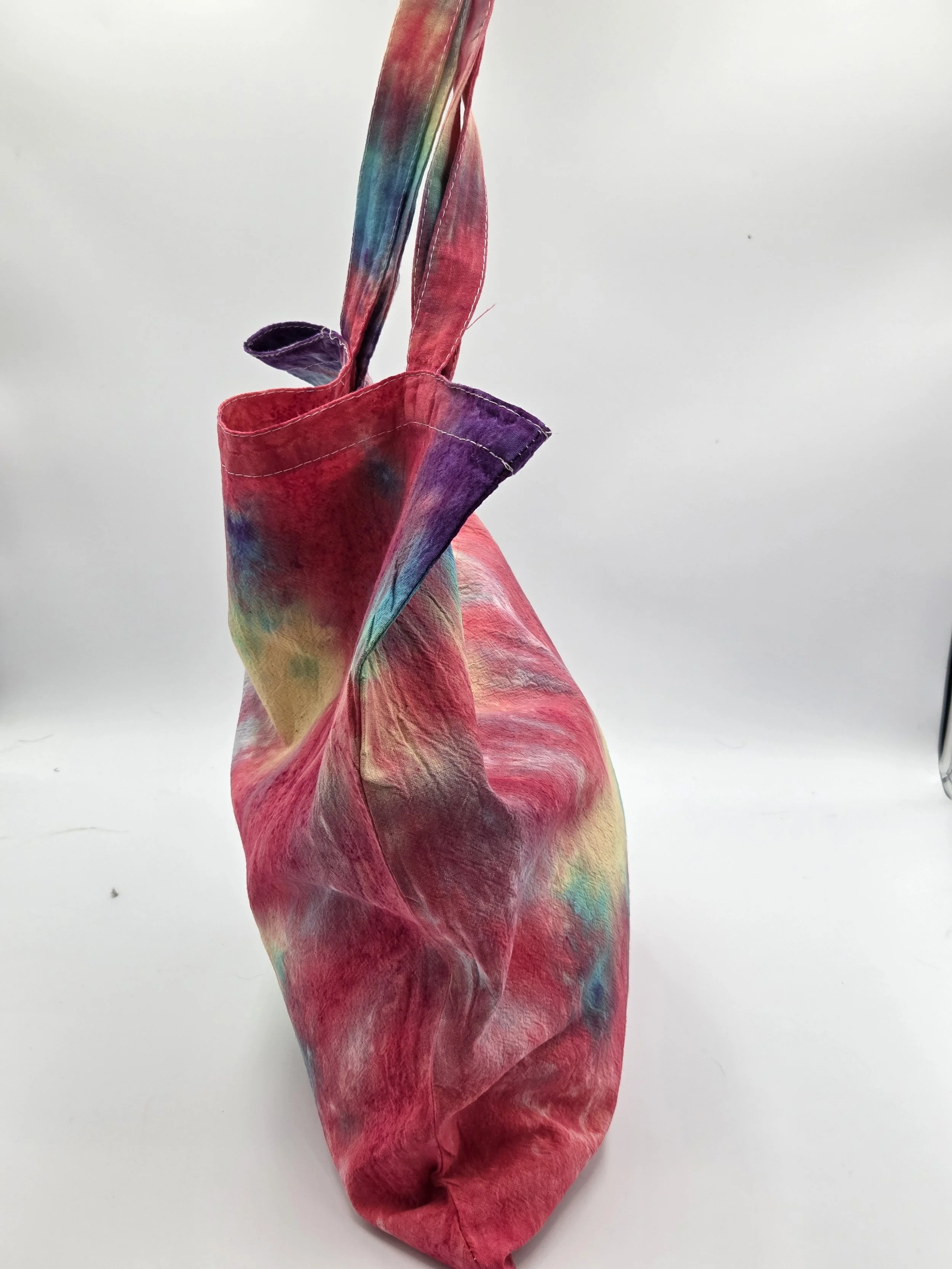 side view A calico tote bag featuring an adaptive tie-dye pattern in coral red, yellow, teal, green, and purple with a playful crab-inspired central motif.