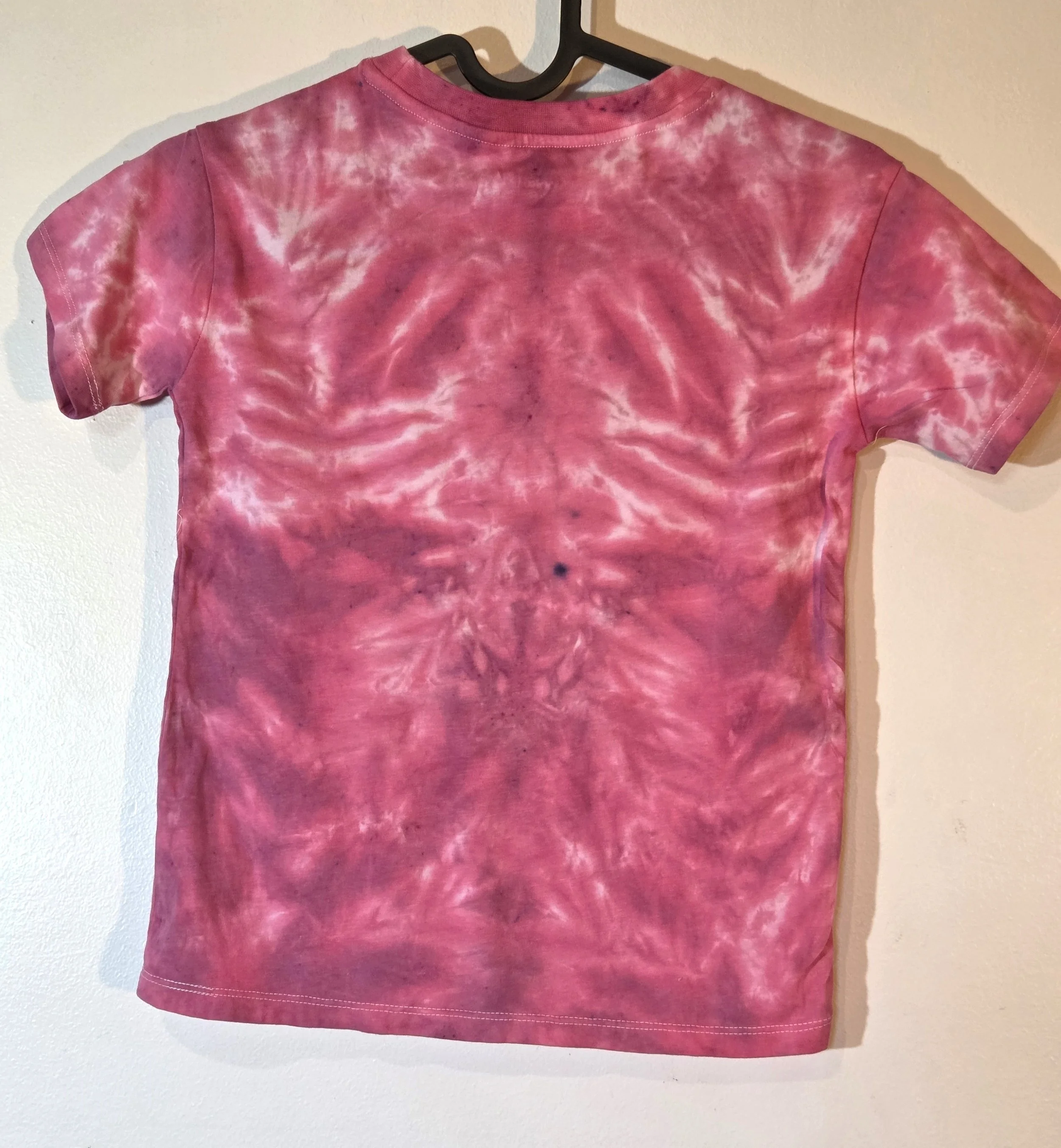 back view of A child's red and burgundy t-shirt featuring a central tie-dye creature pattern with long limbs and white accent streaks.