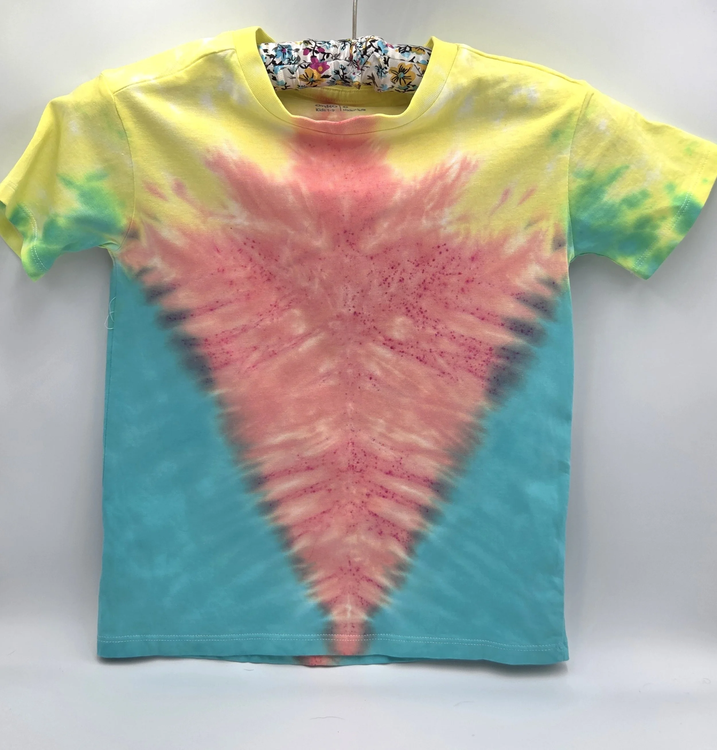 A child's size 6 t-shirt with a half Y-fold tie-dye pattern featuring a central coral V-shape framed by teal sides and yellow shoulders.