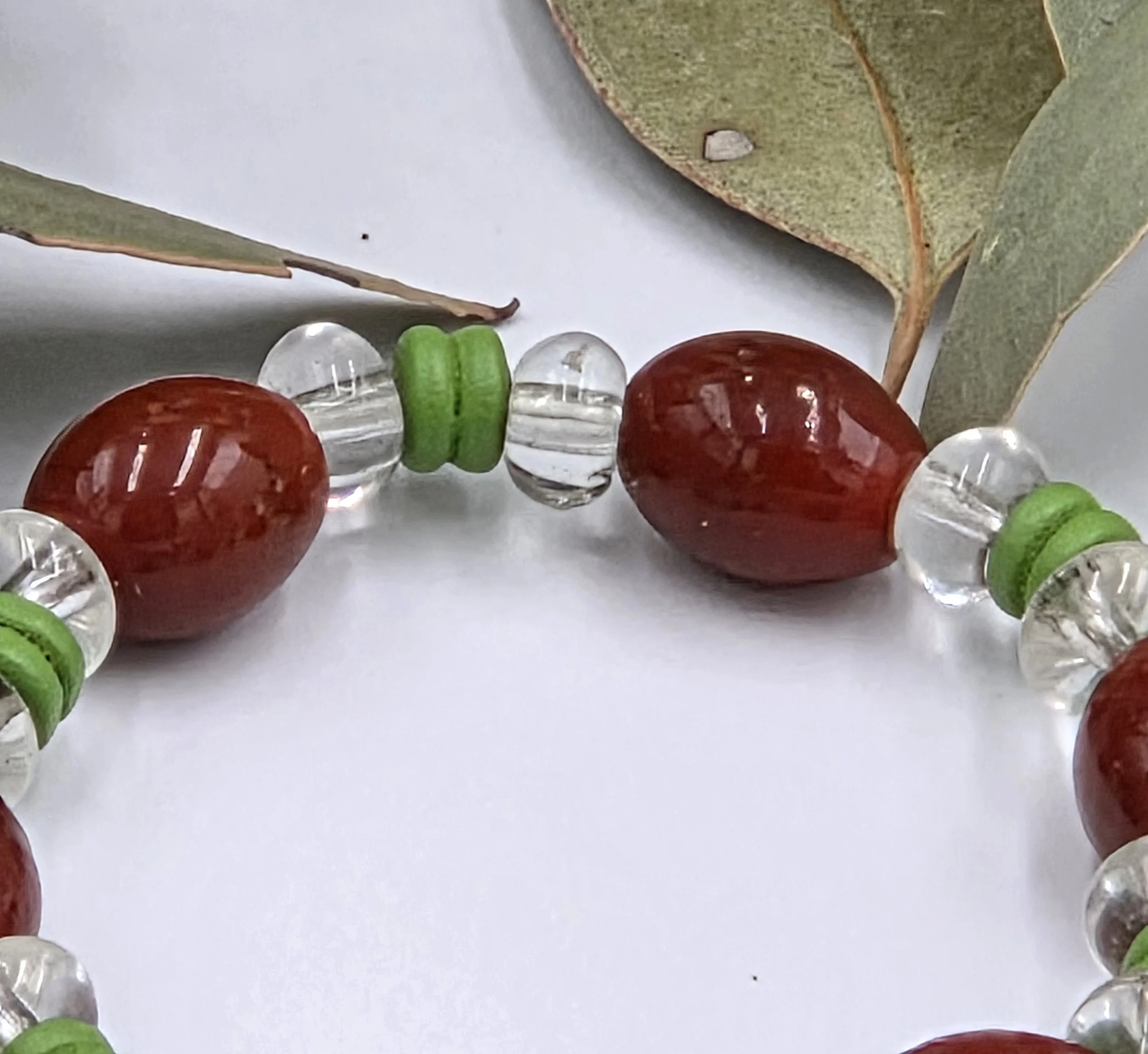 close-up of Rust red glass oval beads separated by clear glass donuts and forest green ribbed wood beads on an elastic bracelet.