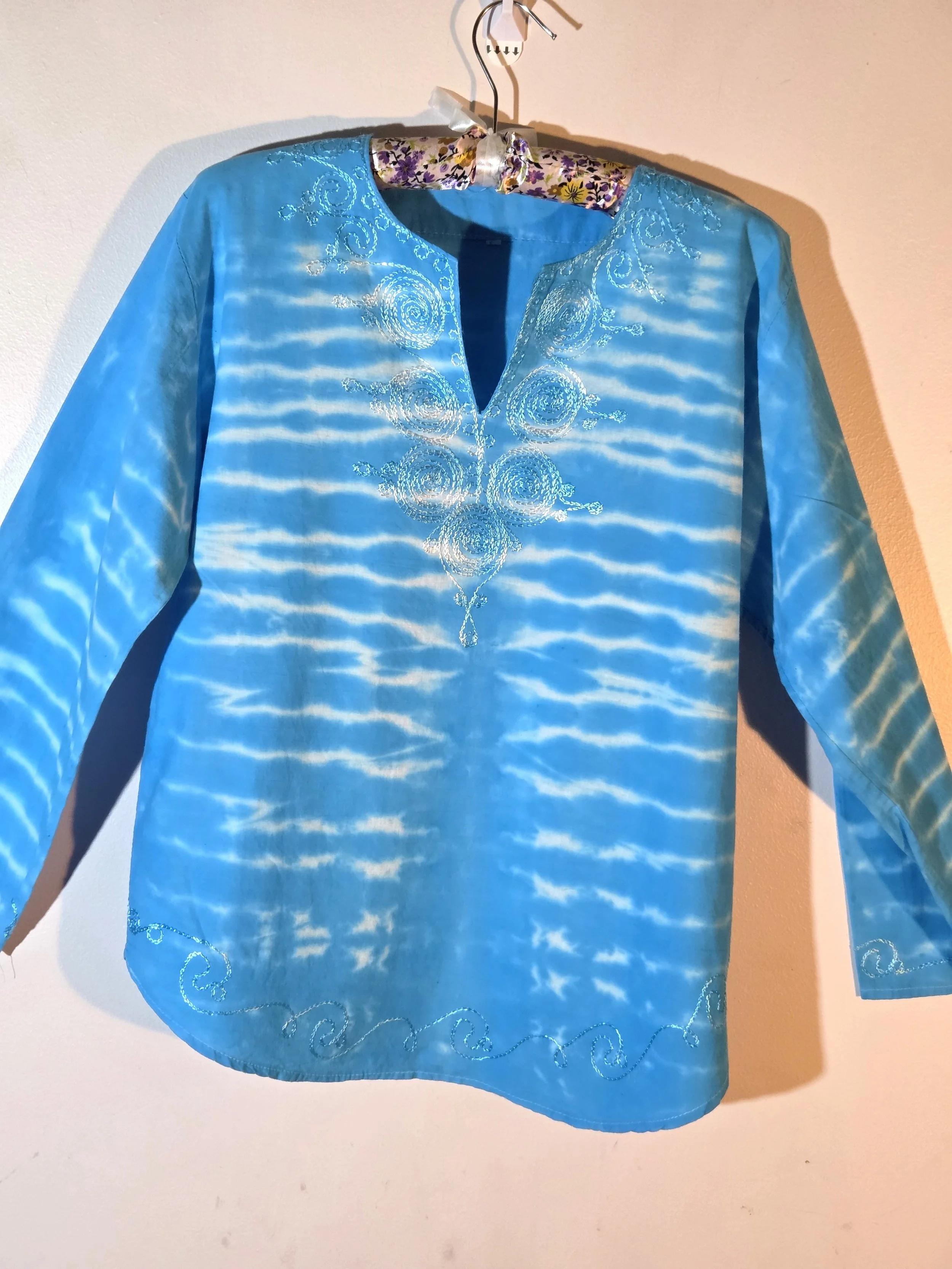 A light blue cotton kaftan shirt with embroidered details, showcasing a vertical tie-dye pattern of thin, wire-like white ripple lines.