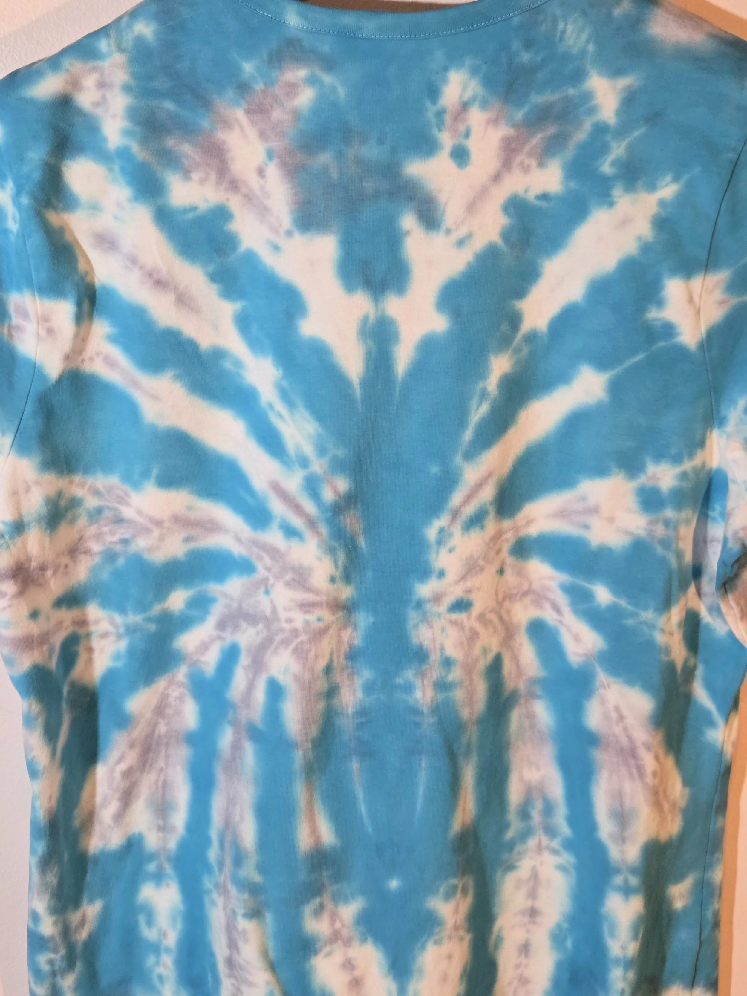 close up back view A size 16 t-shirt featuring a highly defined tie-dye spider pattern in bright aquamarine against a soft grey and white background.