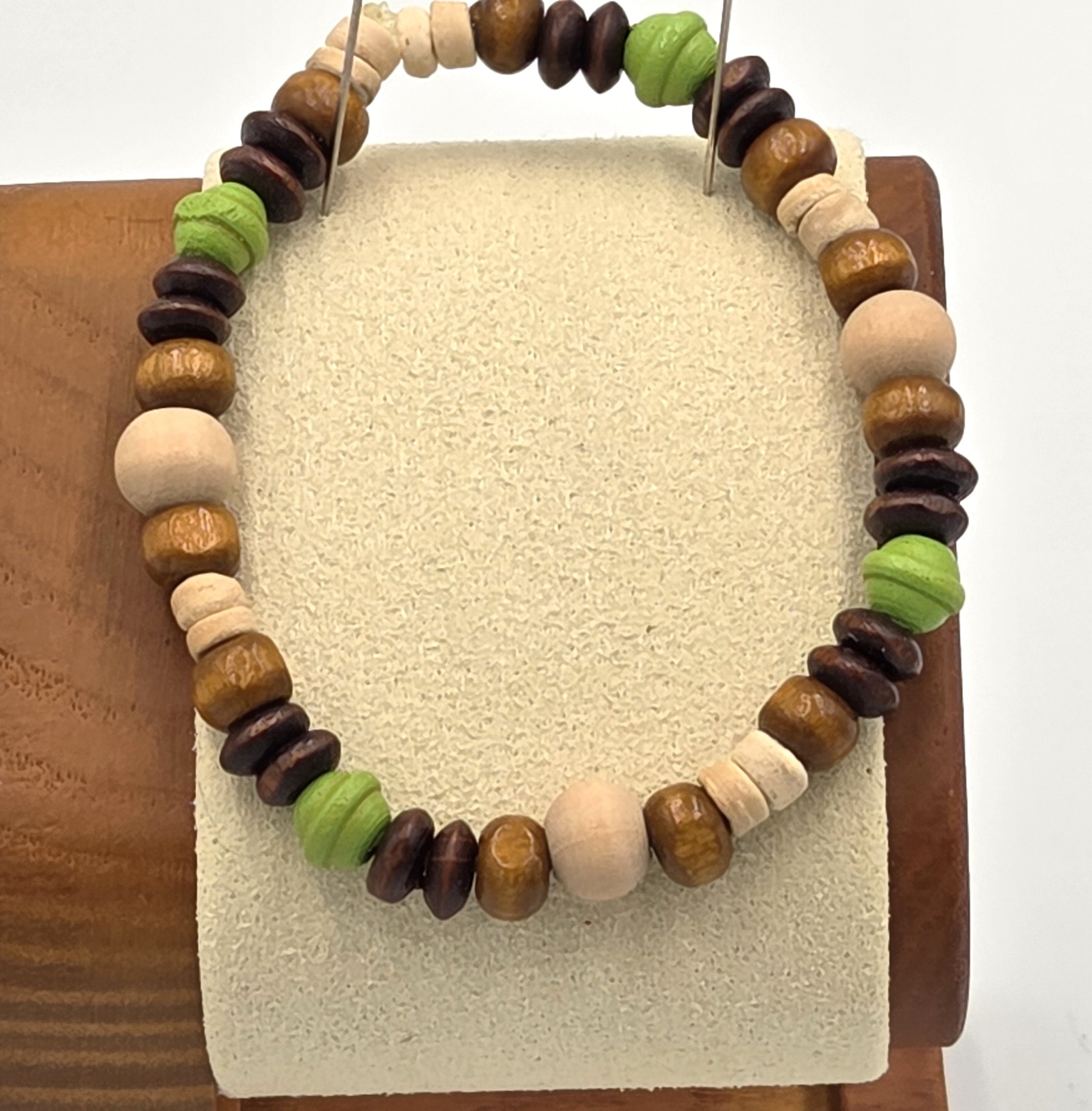 Small elastic bracelet with cream, brown, and lime green wooden beads in varied shapes.