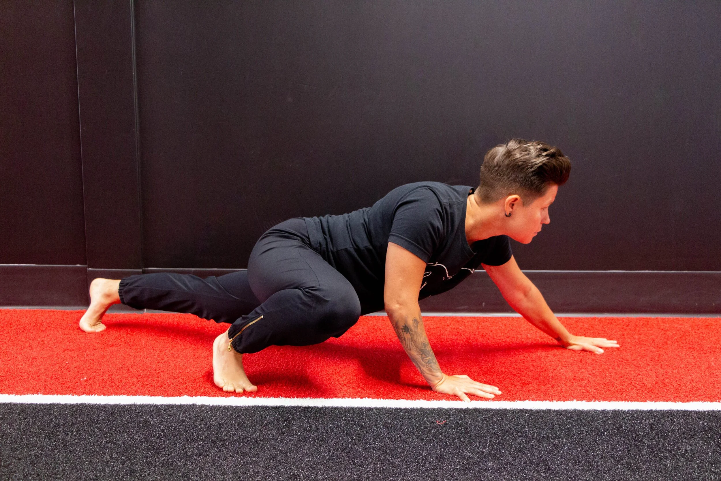 Person in black workout clothes doing a crawl or yoga pose on a red and black gym floor.