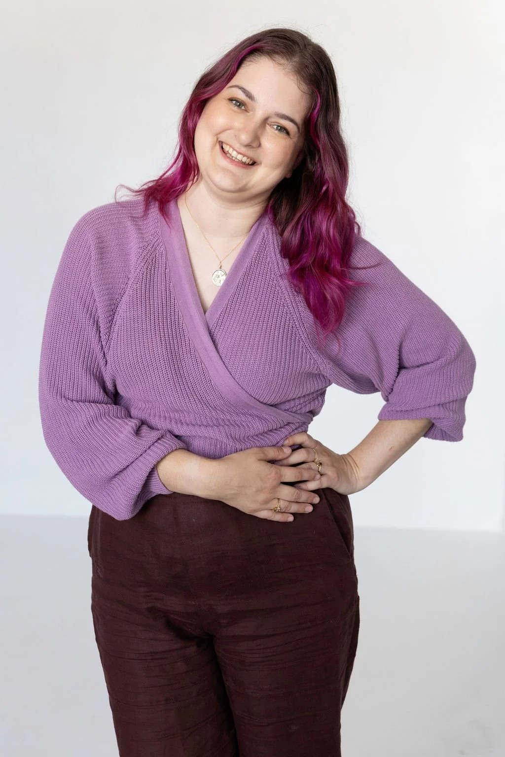 A woman with shoulder-length dark hair smiling and sitting on a yellow chair, wearing a white shirt and blue jeans, in a well-lit room.