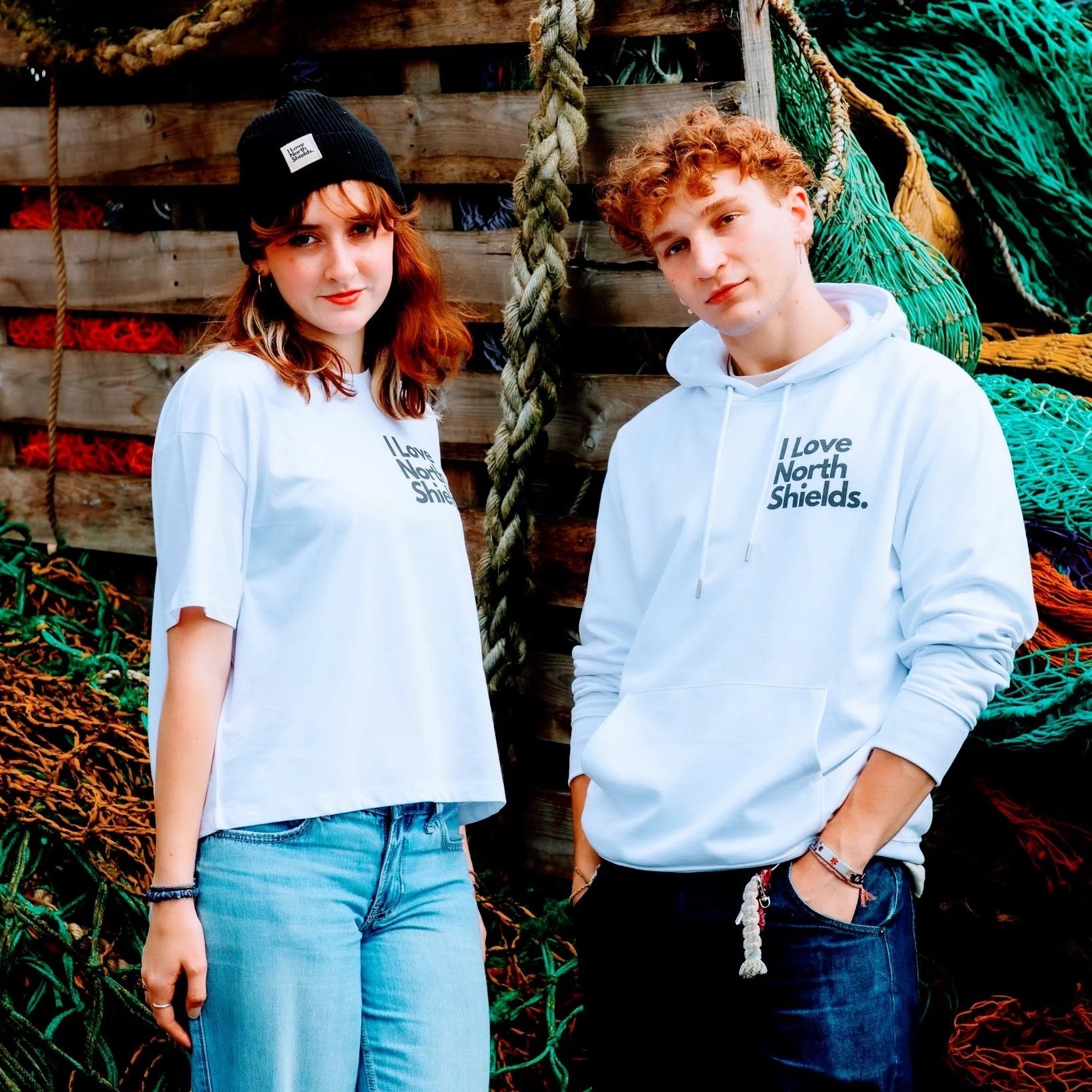 Two young people, standing outdoors in North Shields, wearing 100% organic cotton garments. They are part of the I Love North Shields magazine community and are wearing merchandise printed by sustainable garment printing studio Lyoness Press.