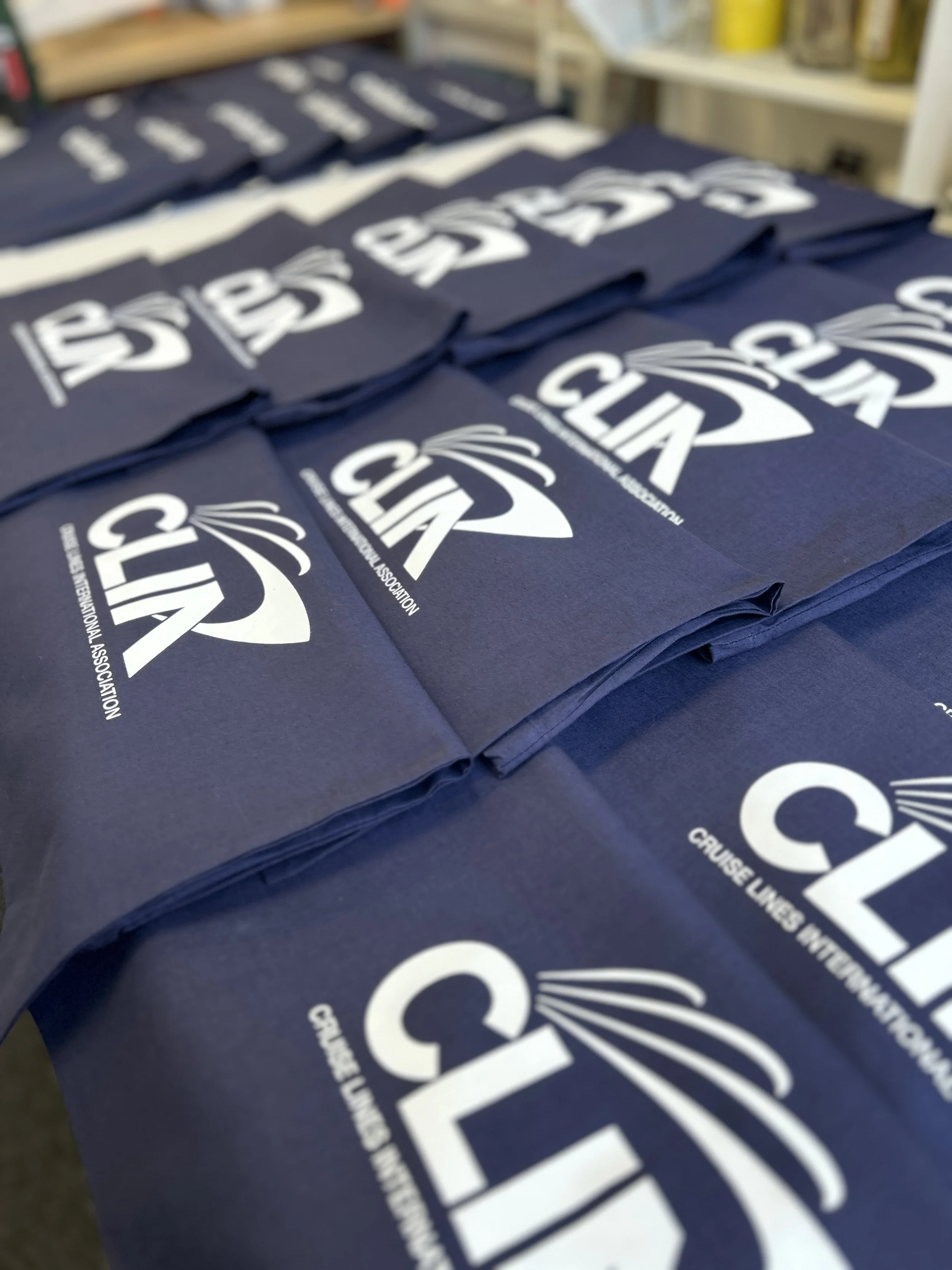 Blue Earth Positive tote bags with white logo and text for the International Association of Cruise Lines, arranged in stacks.