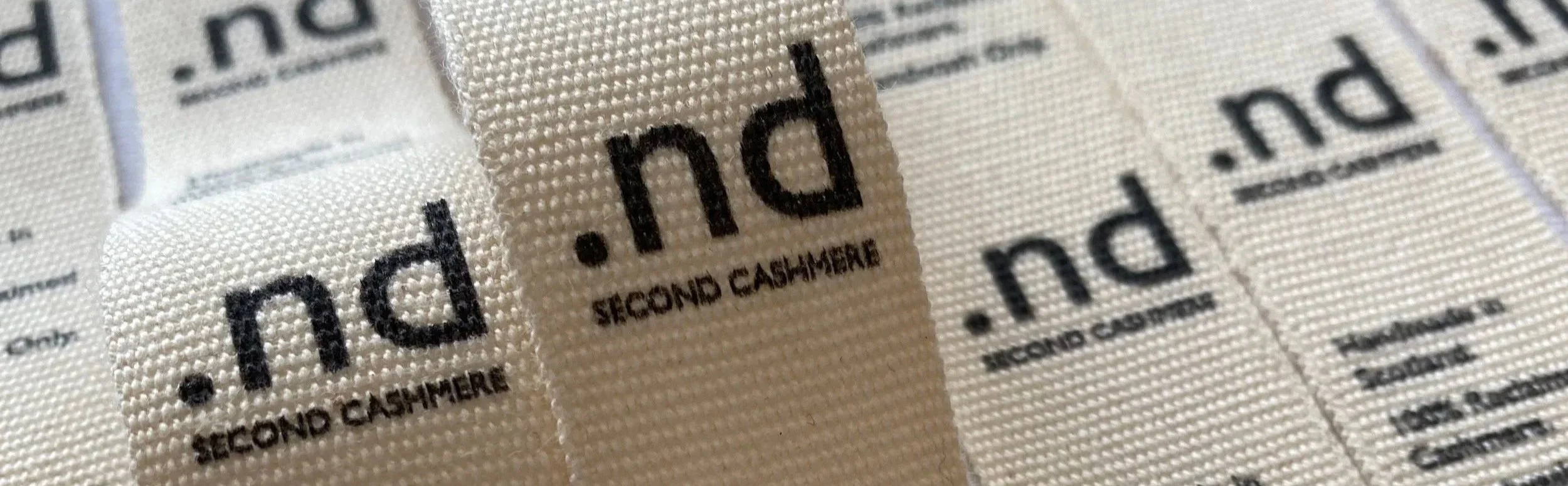 Close-up of fabric tags with black printed text reading 'SECOND CASHMERE' on 100% organic cotton tape.