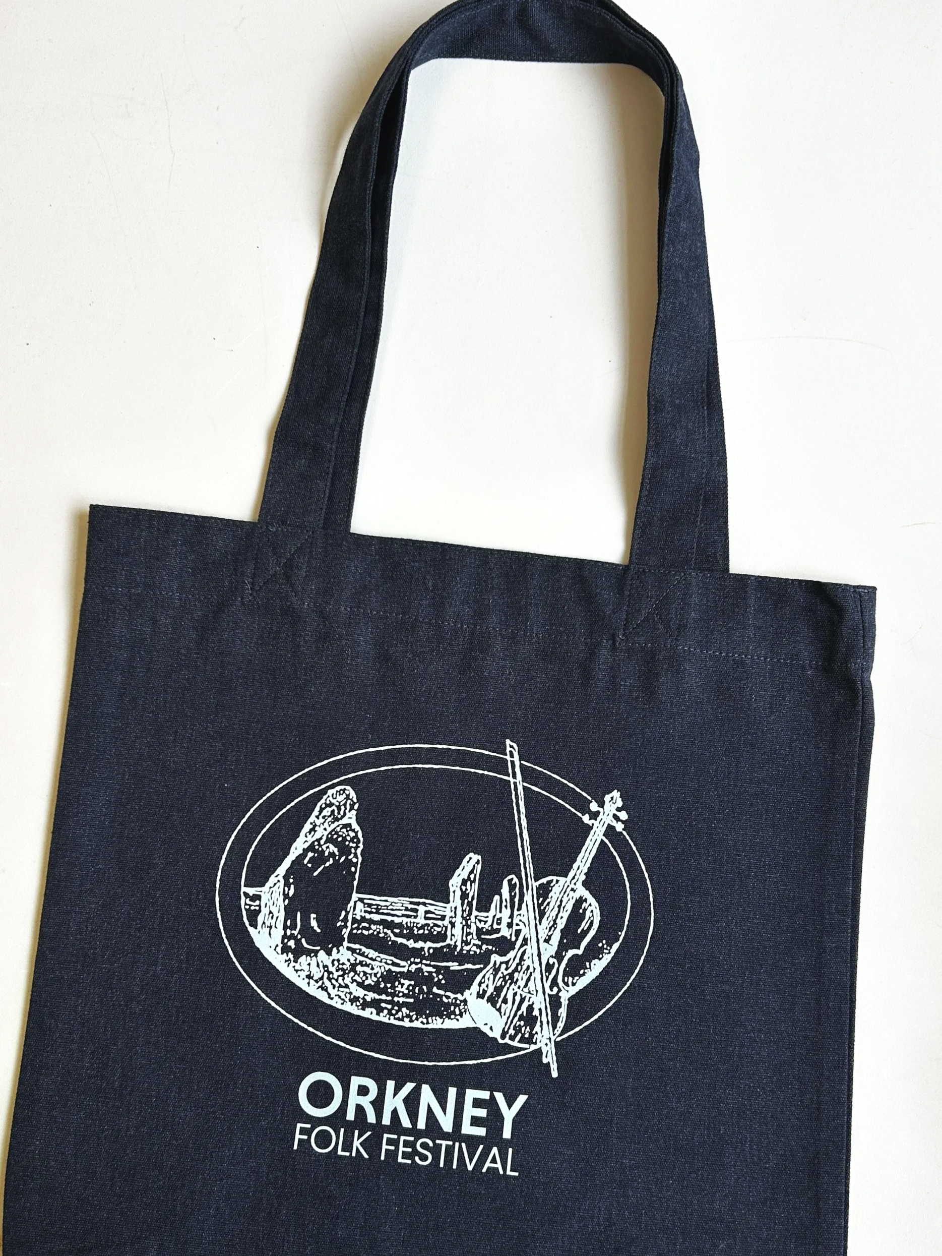 Black tote bag with white graphic and text for the Orkney Folk Festival, featuring a circular design with musical instruments and the festival's name.