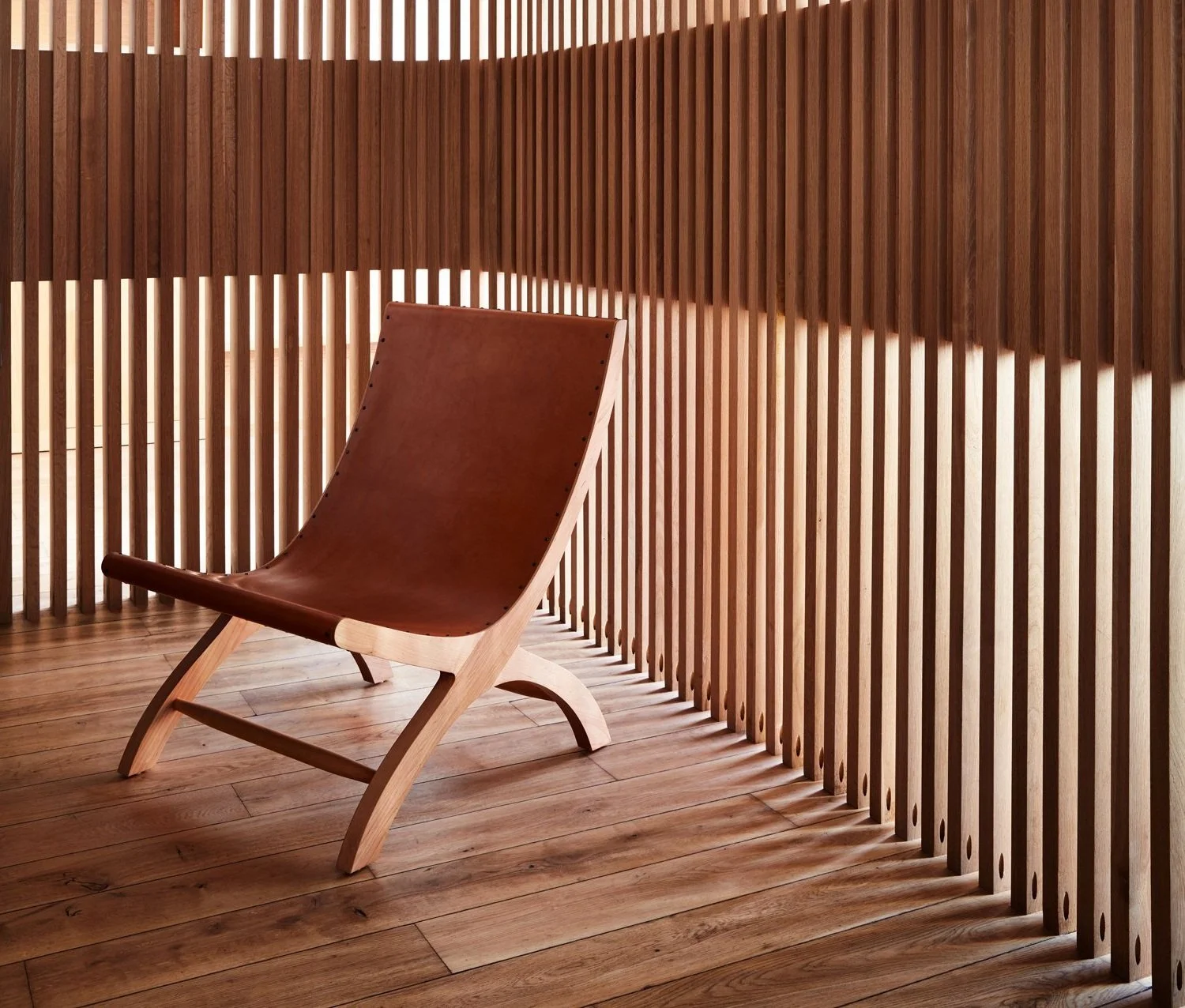 A modern wooden chair with a leather seat in a room with wood-paneled walls and flooring.
