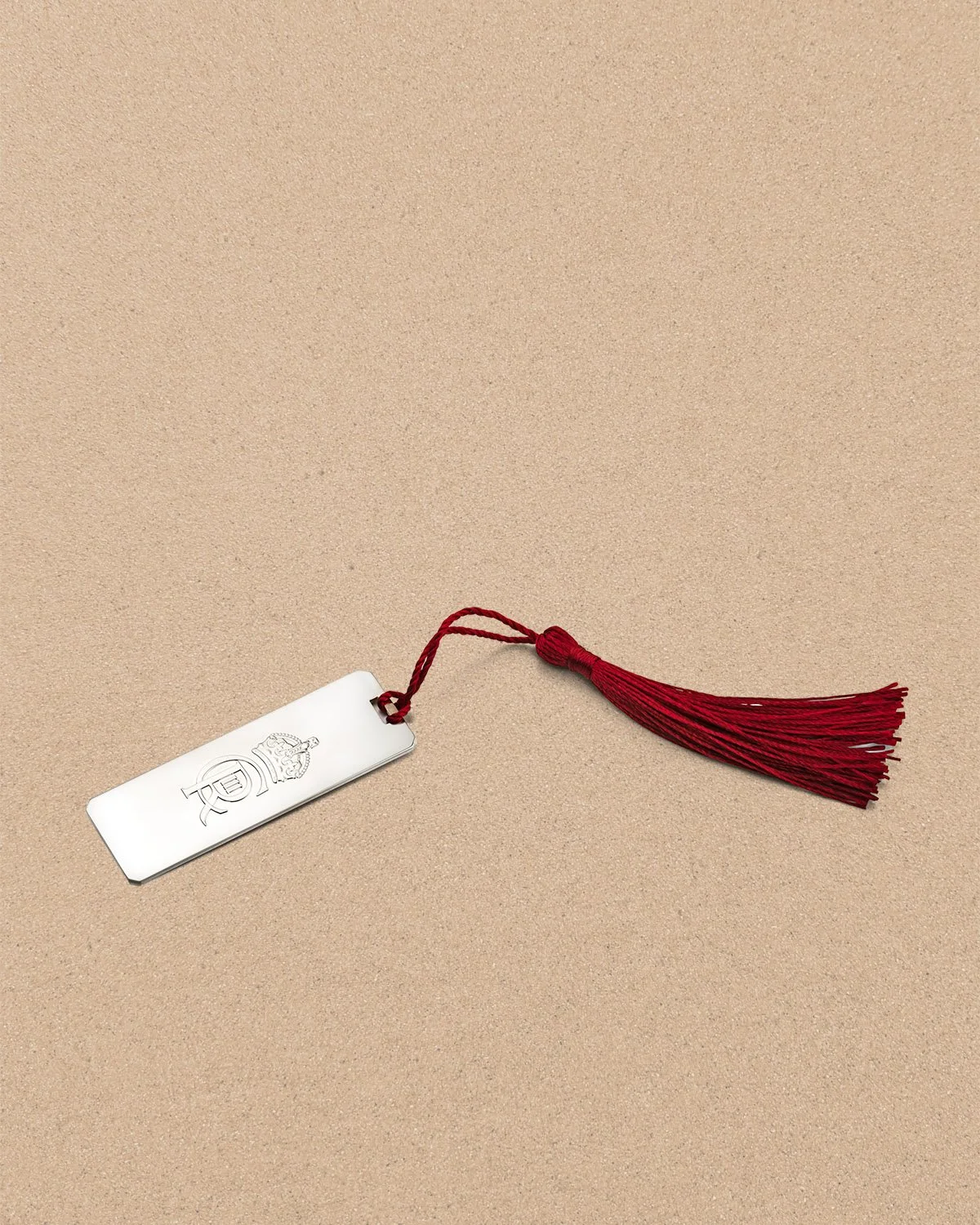 A silver bookmark with a red tassel on a beige surface.
