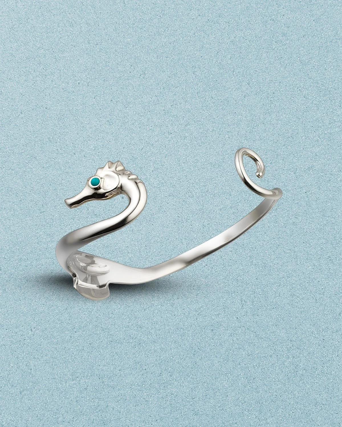Silver swan-shaped jewelry holder with a turquoise eye, placed on a light blue textured background.
