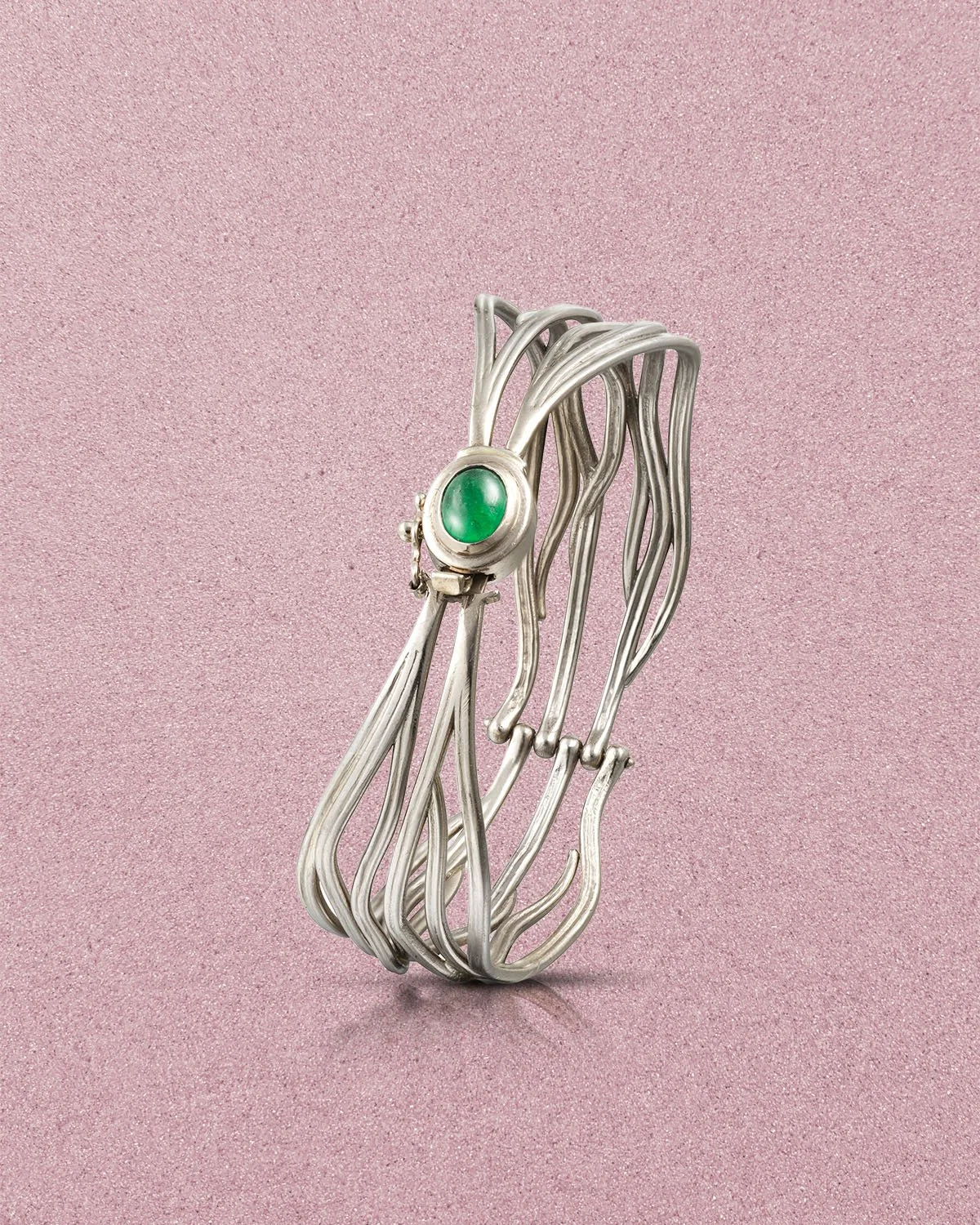 Silver wire bracelet with a green stone setting on a pink textured background.