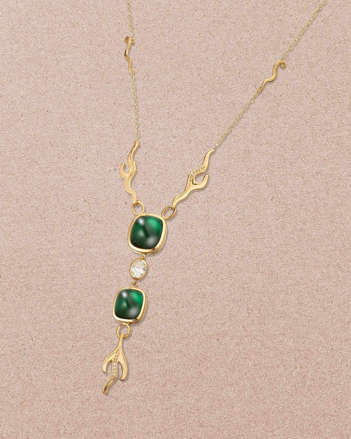 Gold necklace with green stones, a small clear gemstone, and flame-shaped decorative elements on a beige background.