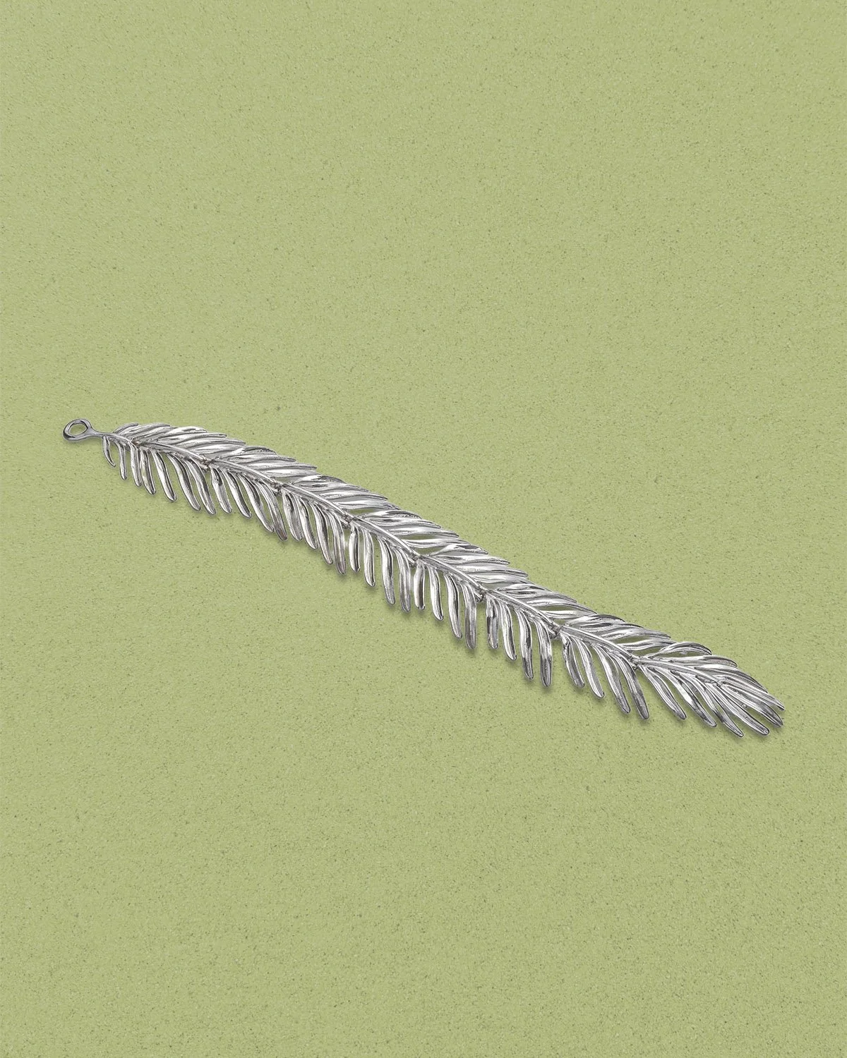 Silver palm leaf statement bracelet on light green background.
