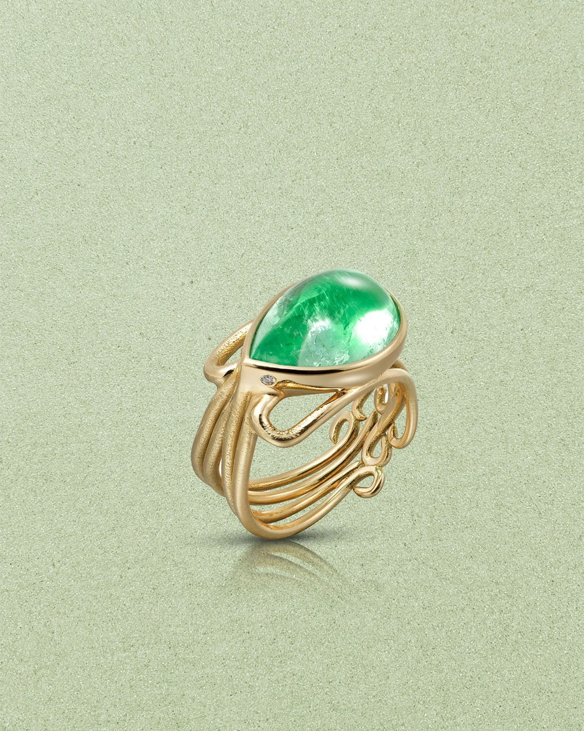 Gold ring with an oval green gemstone on a light green textured background.