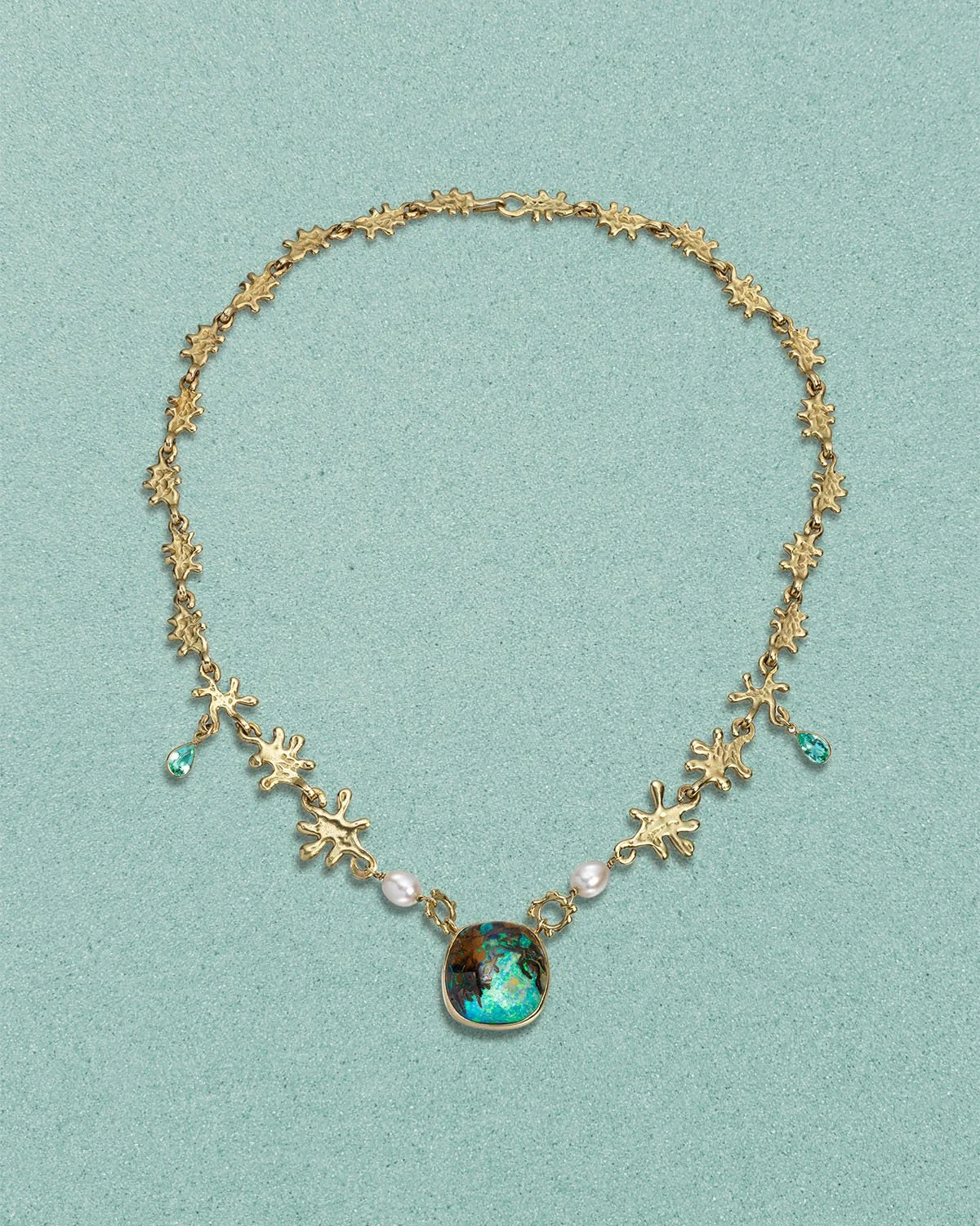 Gold necklace with a central opal, pearl accents, and turquoise teardrop charms, on a light green background.