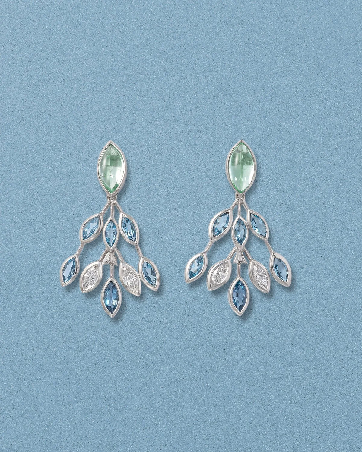 Pair of silver earrings with green, blue, and clear gemstones arranged in a leaf pattern, displayed on a light blue background.